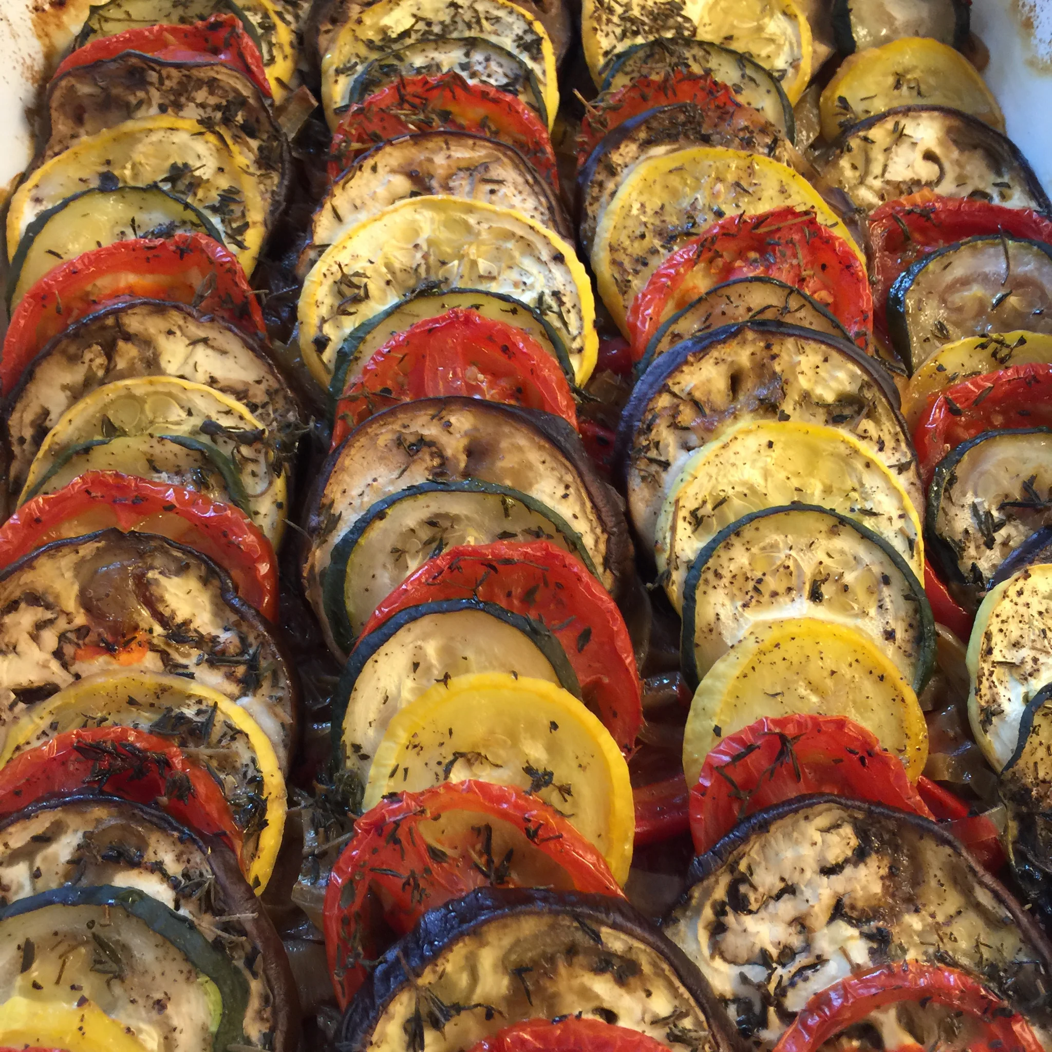 Close-up view of roasted zucchini and red and yellow bell peppers seasoned with herbs.