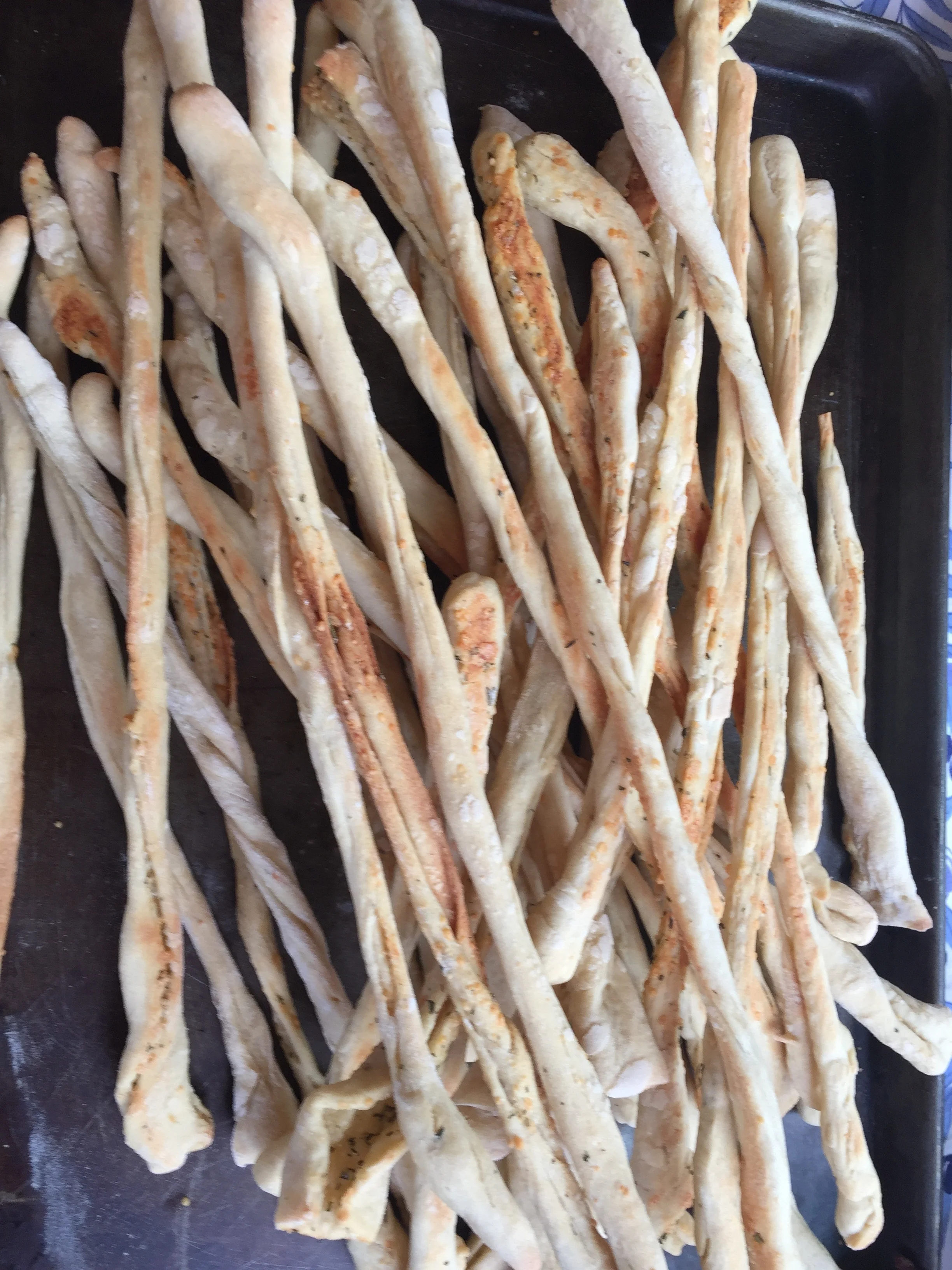 Frozen breadsticks on a black baking sheet.
