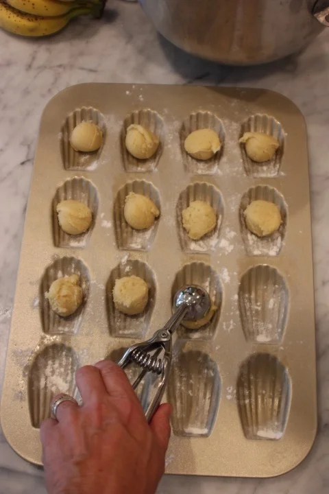 Hand using an ice cream scoop to shape cookie dough into balls in a baking tray lined with parchment paper.