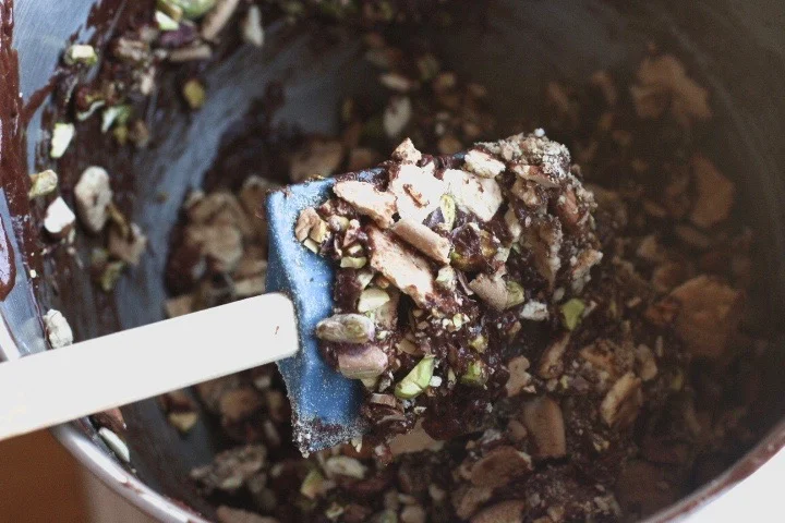 Close-up of a spatula holding crushed pistachio nuts inside a metal container with more crushed pistachios scattered around.