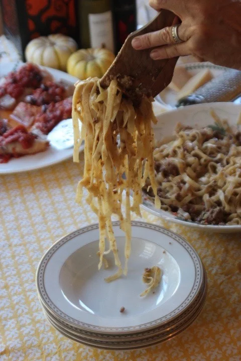 Hand serving fettuccine pasta from a pan onto a plate in a home kitchen.