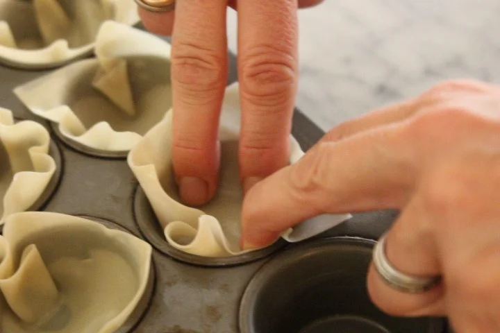 Someone pressing on homemade pasta dough using a round cutter in a muffin tin.