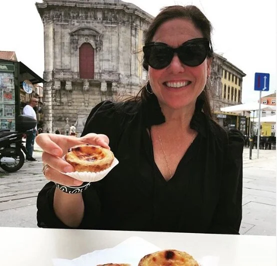 Woman smiling and wearing sunglasses holding a small pizza outdoors in a historic city square.