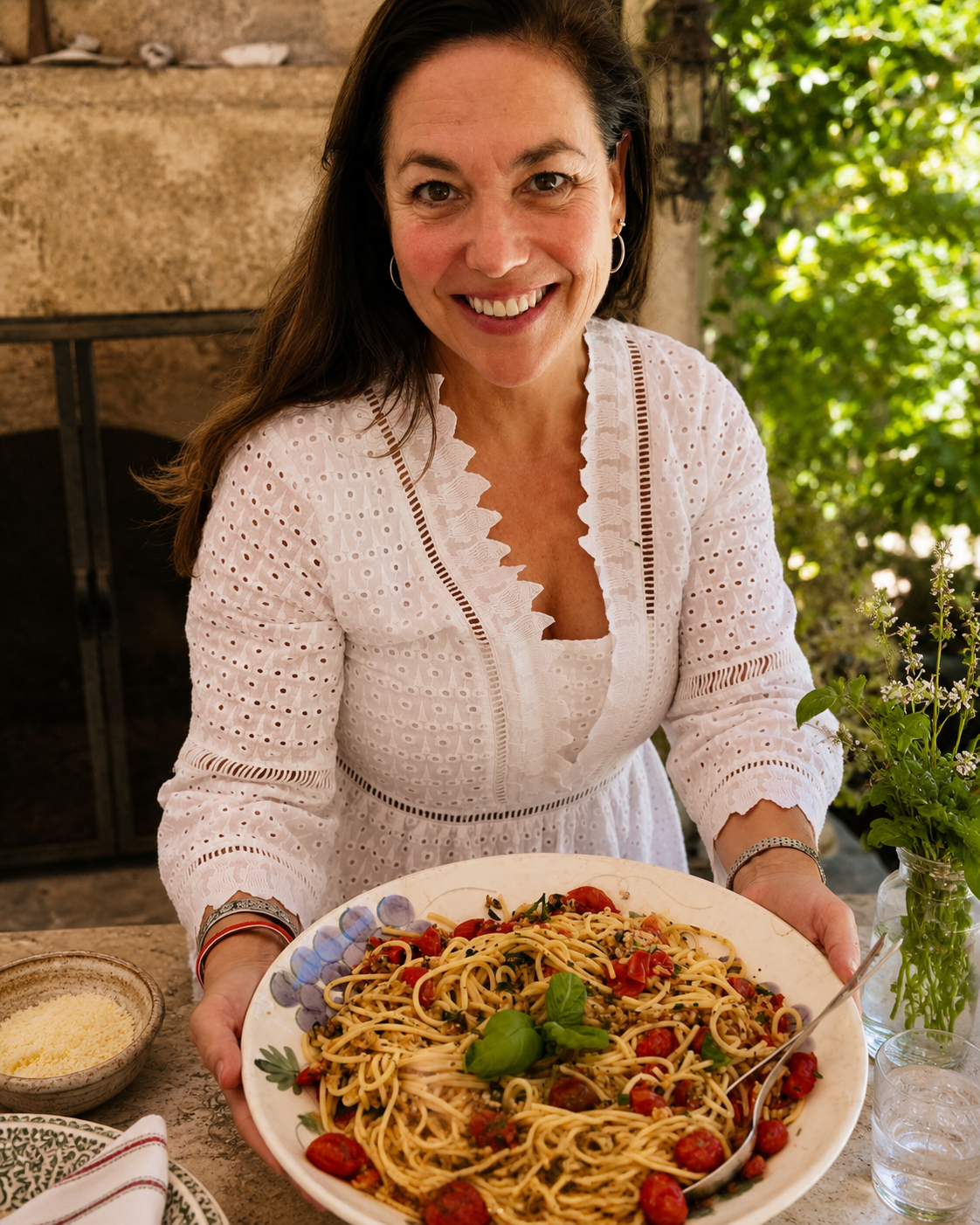Woman holding a plate of spaghetti with cherry tomatoes and basil, smiling at the camera.