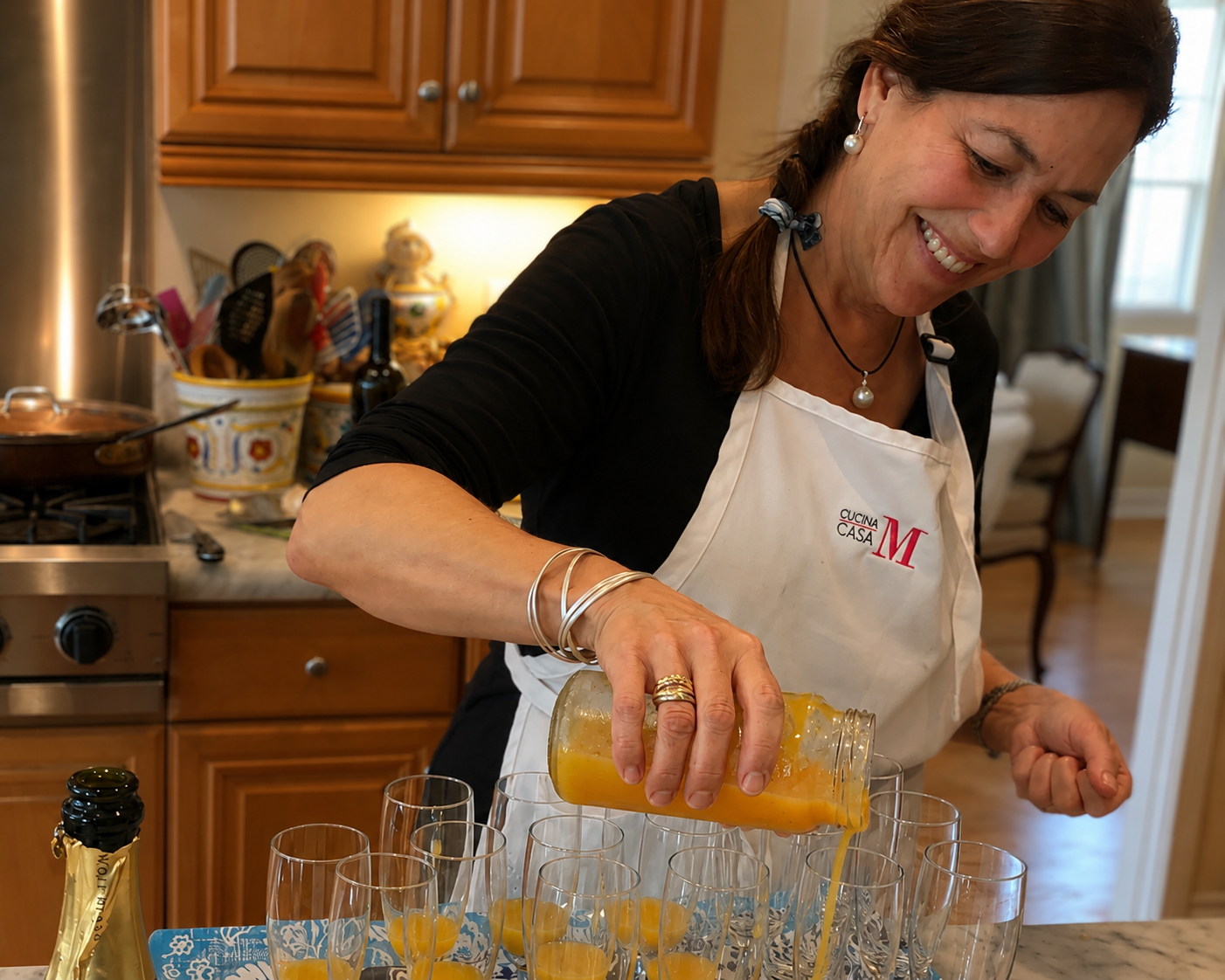 A woman in a white apron pouring a yellow drink into glasses in a kitchen.