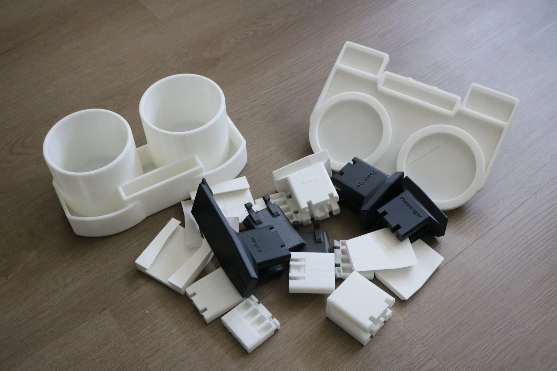 Disassembled white plastic parts and black electrical connectors on a wooden floor.
