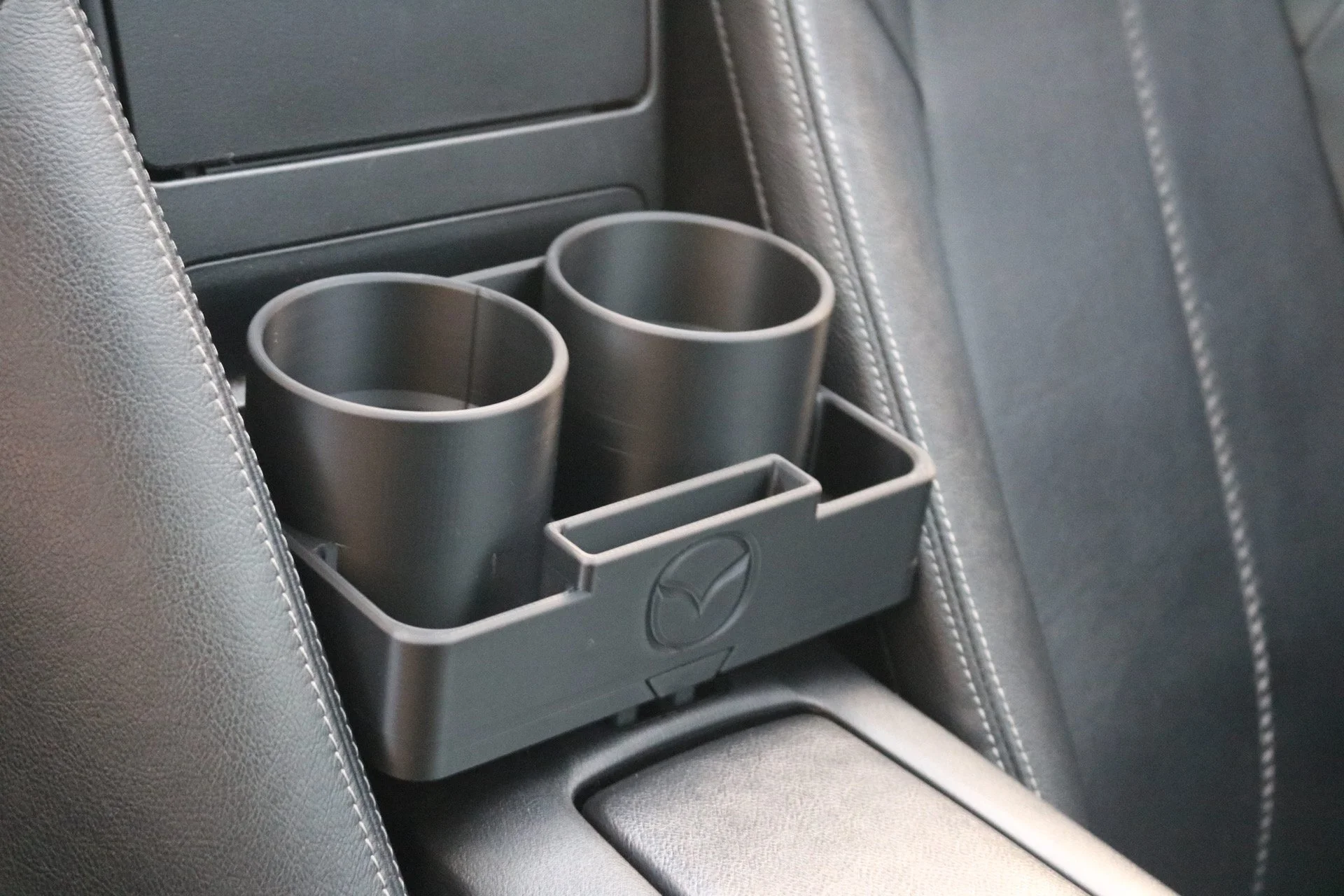 Car seat back with a Mazda-branded cup holder containing two empty stainless steel cups.
