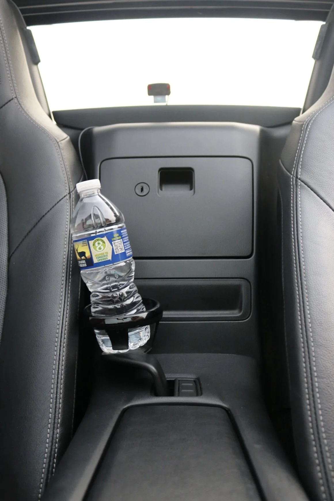 View of the backseat area of a vehicle showing a water bottle secured in a cup holder between the seats, with the car's interior and a rear window visible.