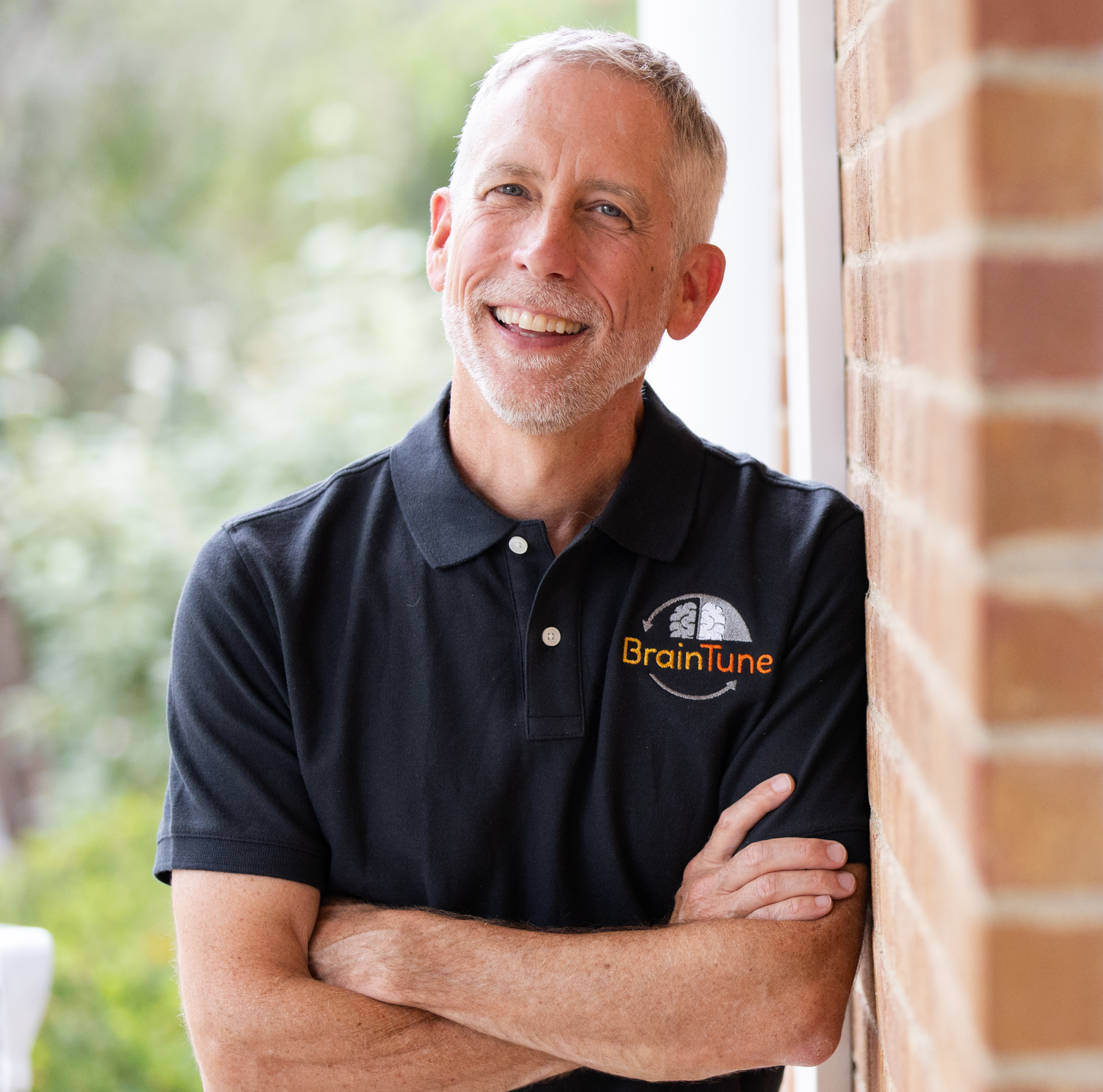 Headshot of team member wearing a dark gray/black shirt smiling with his arms crossed