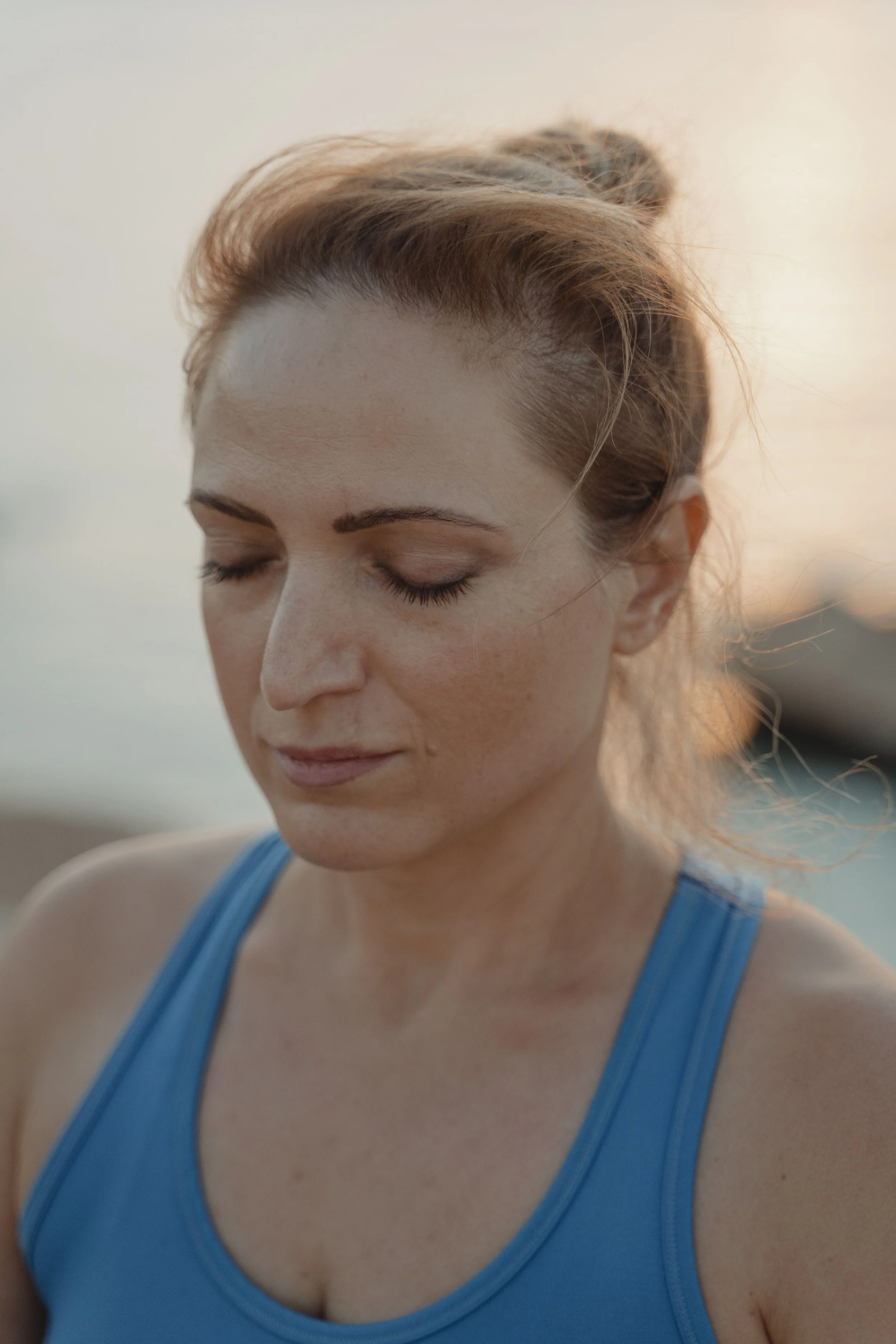 image of women with her hair up in a blue tank top with her eyes closed