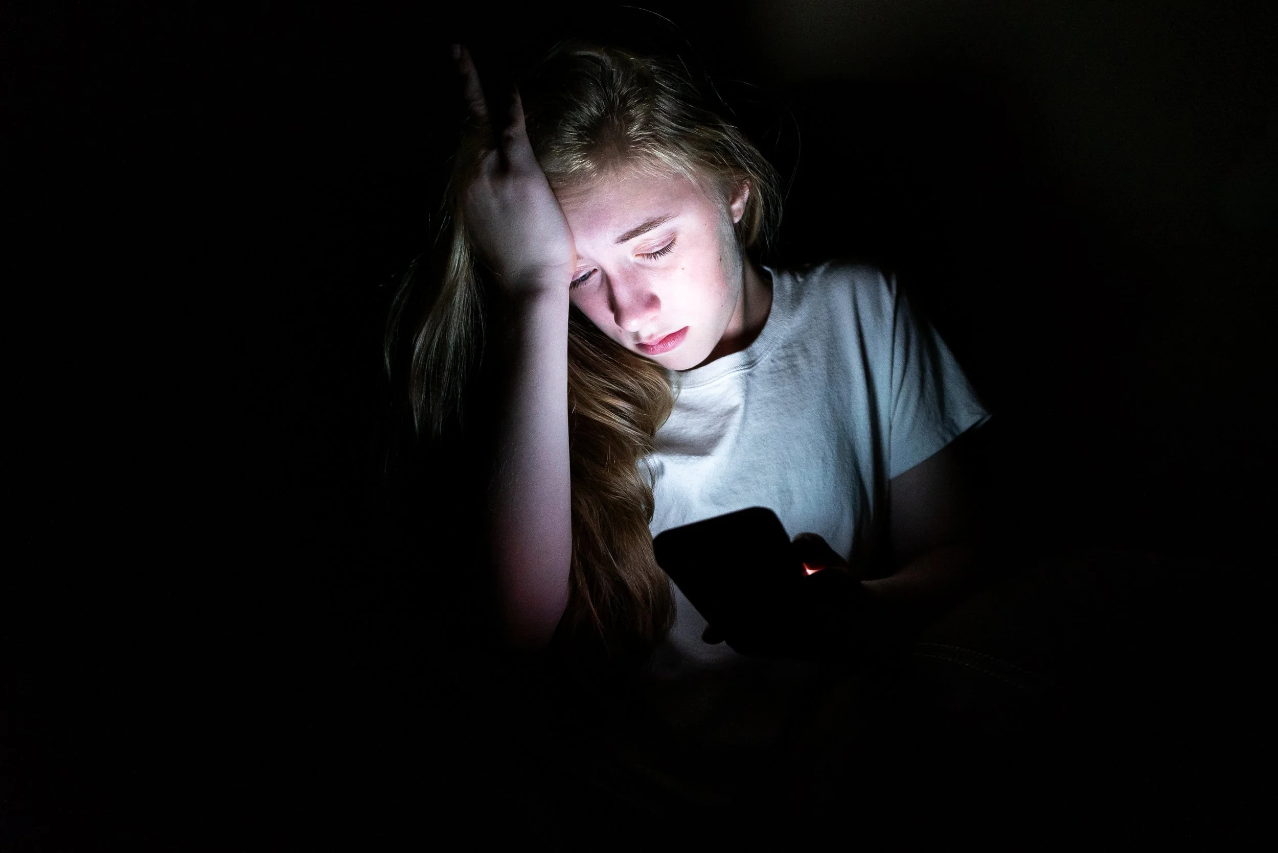teenager in the dark looking stressed at her phone