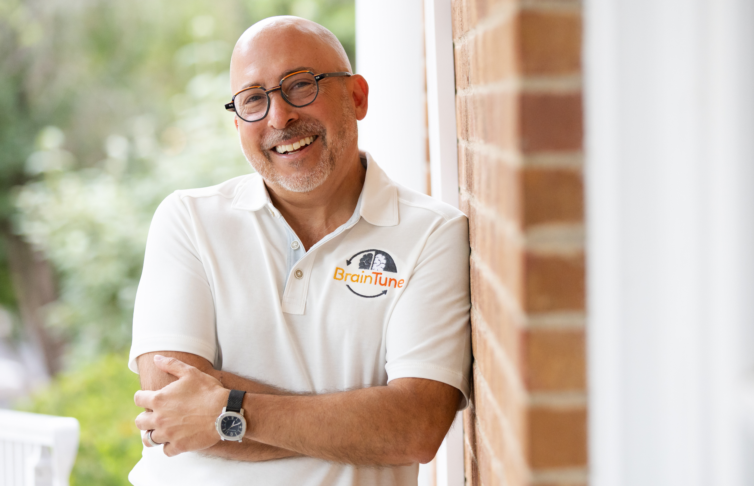 Headshot of a bald man in glasses wearing a white shirt with his arms crossed