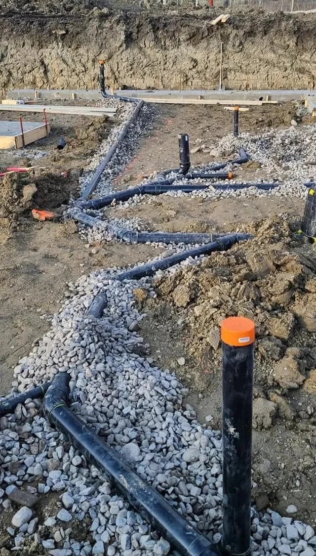 Construction site with underground piping, gravel, and concrete foundation outlines