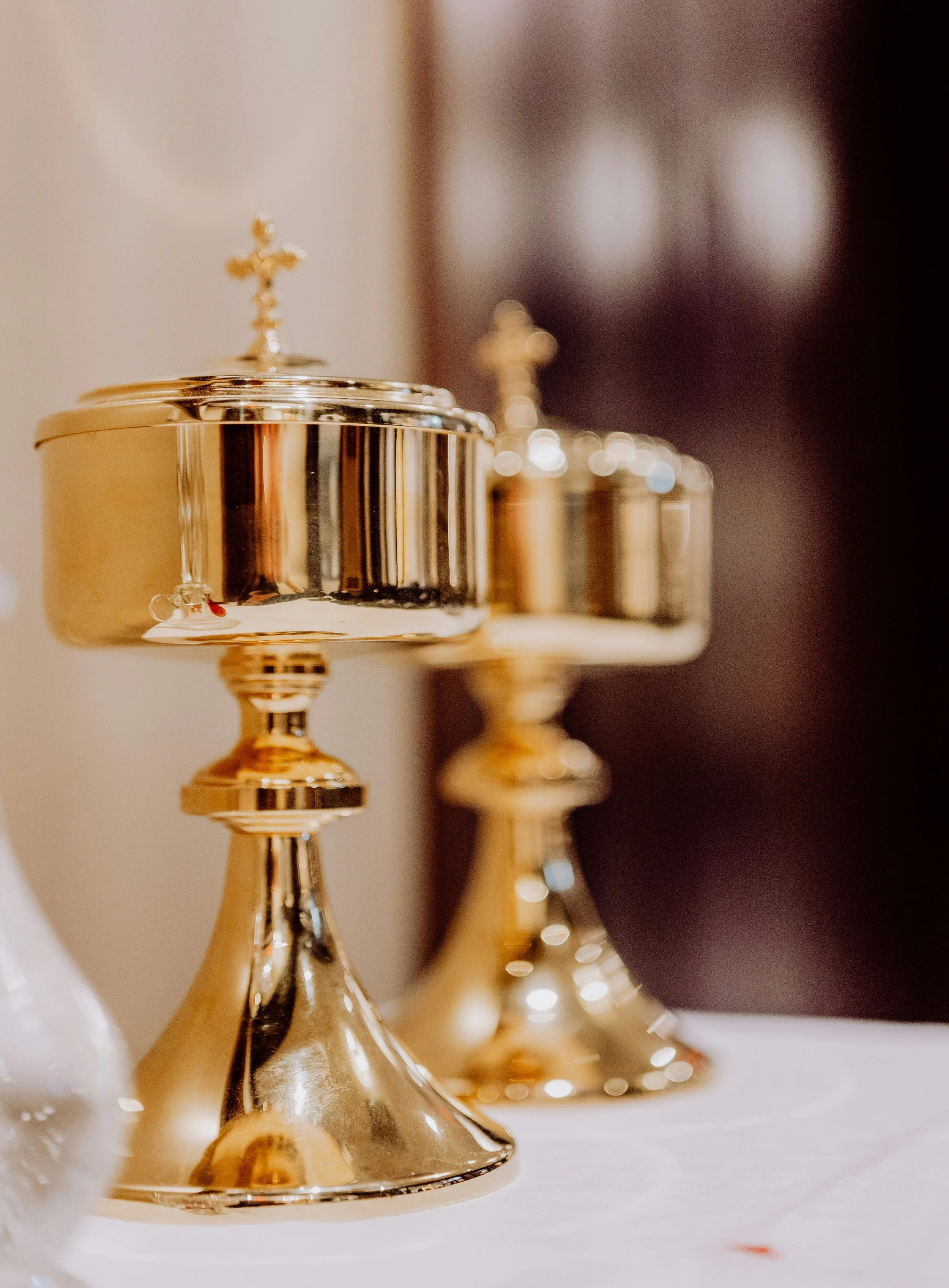 A row of gold chalices with crosses on top, placed on a white surface, with a dark background.