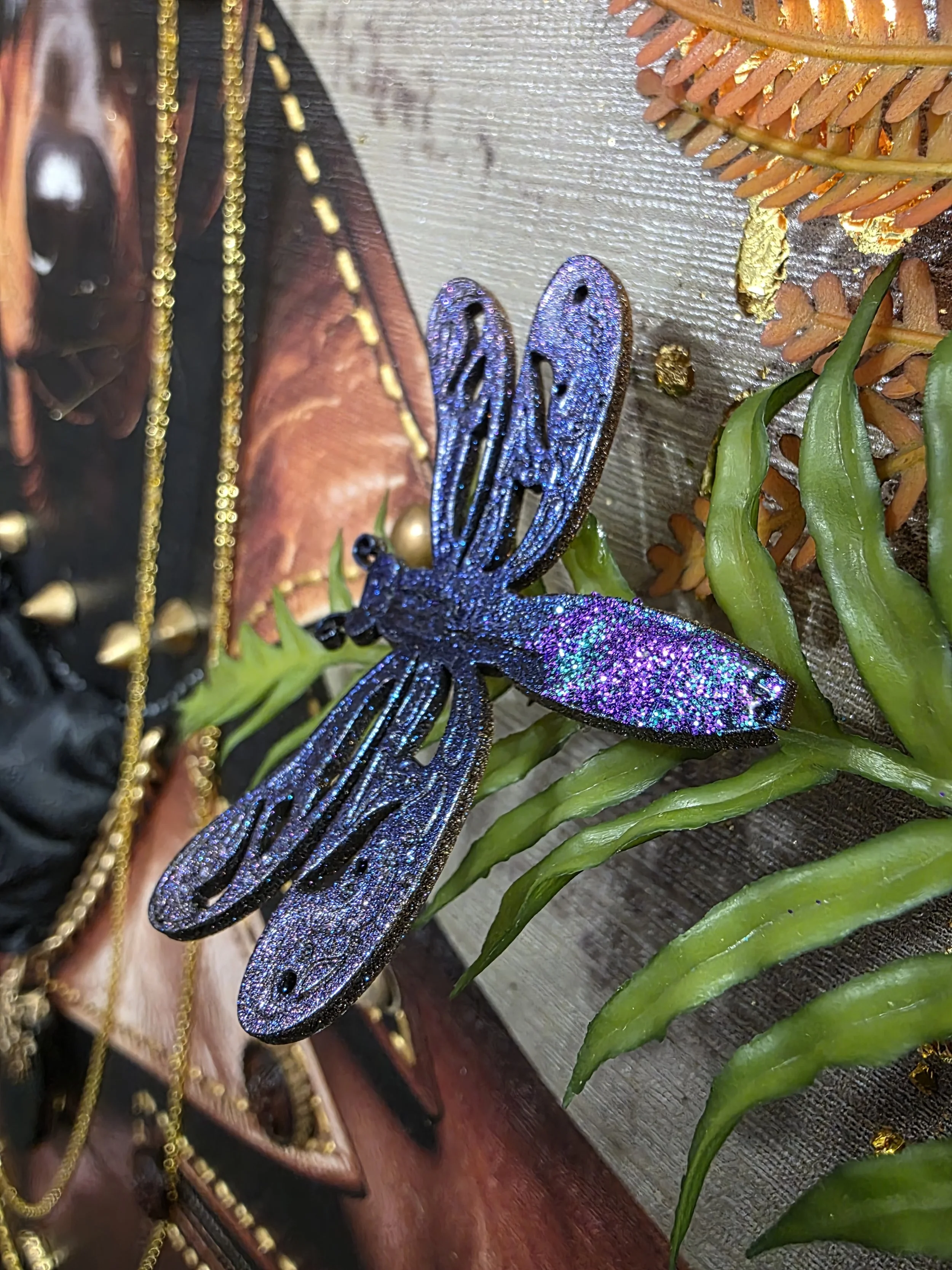 Close-up image of a colorful decorative plant with purple, glittery butterfly and green leaves, positioned on a wooden surface.