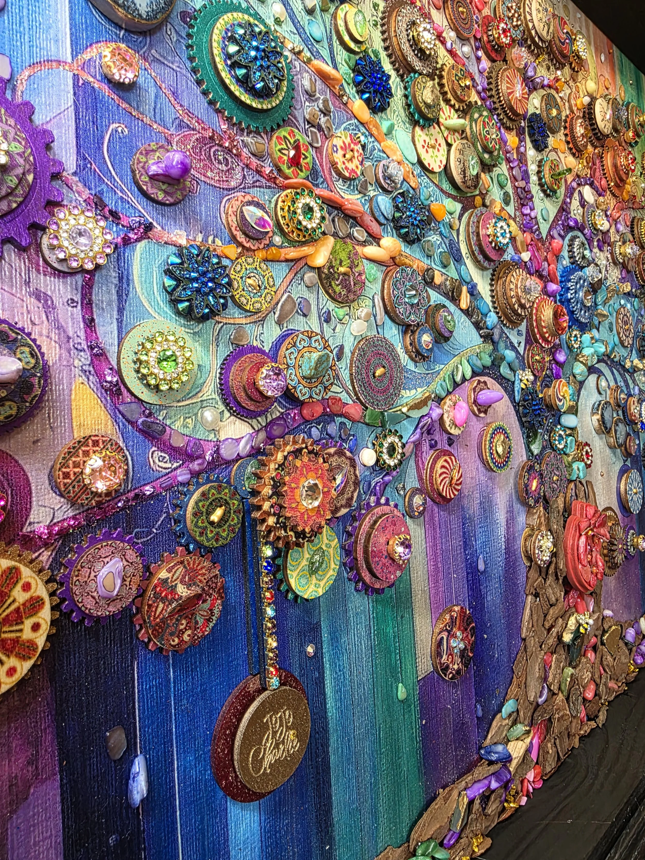 Colorful mixed media art piece with various small objects, beads, and jewelry on a vibrant rainbow background, creating a textured collage.