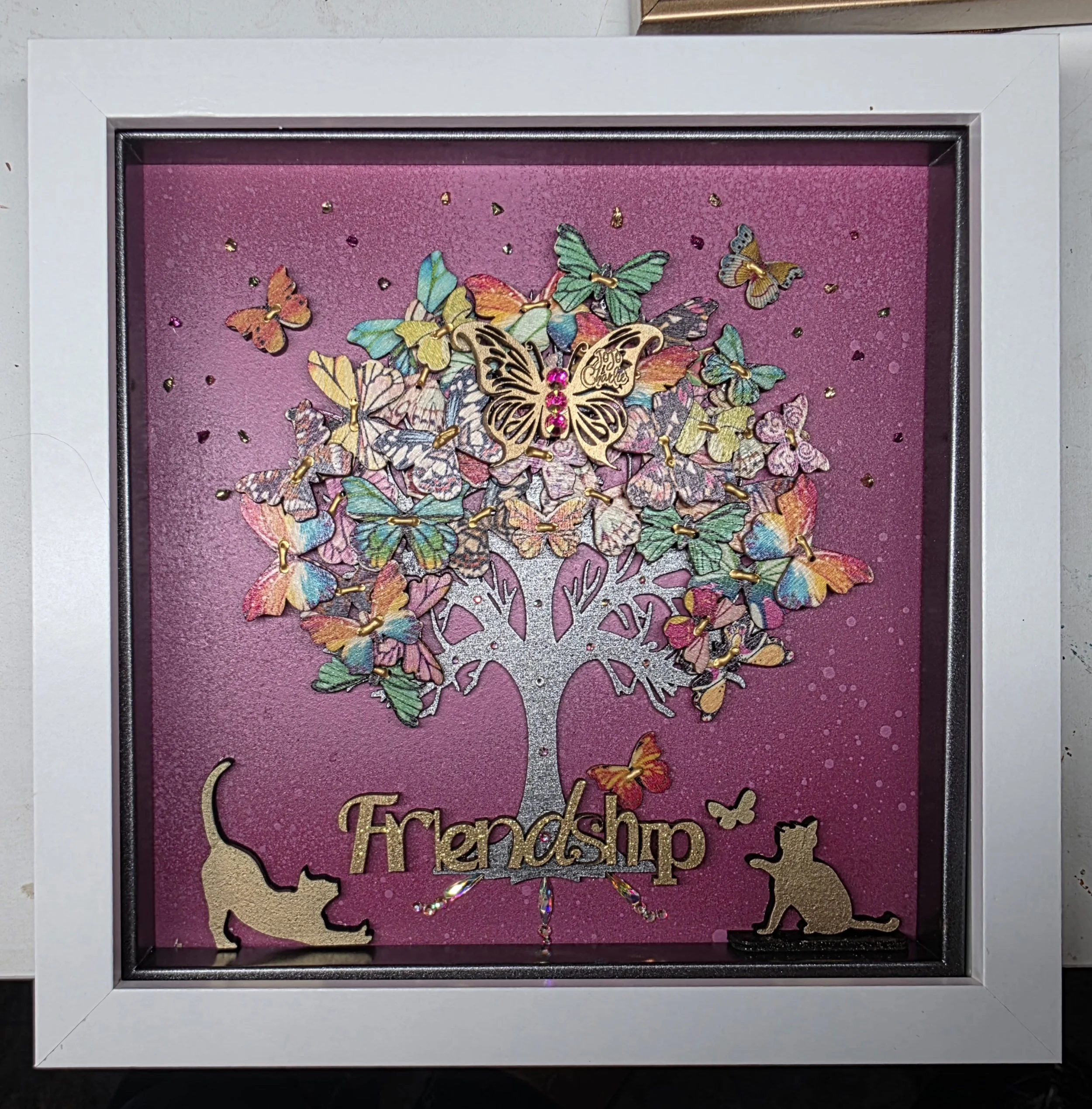 Decorative shadow box featuring a wooden cut-out of the state of Texas with the words 'Fremdsch' underneath, filled with numerous colorful butterfly embellishments on a pink background.
