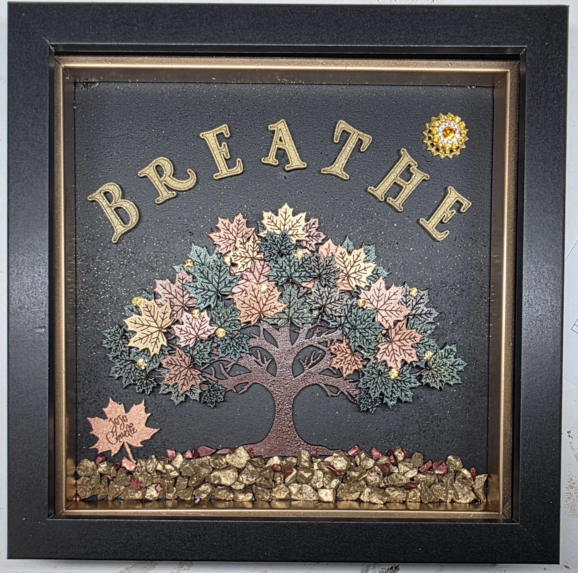 Decorative framed artwork featuring a autumn leaf motif with the words "Blessed" in gold glittery letters, surrounded by artificial leaves, gold rocks, and small gemstones.