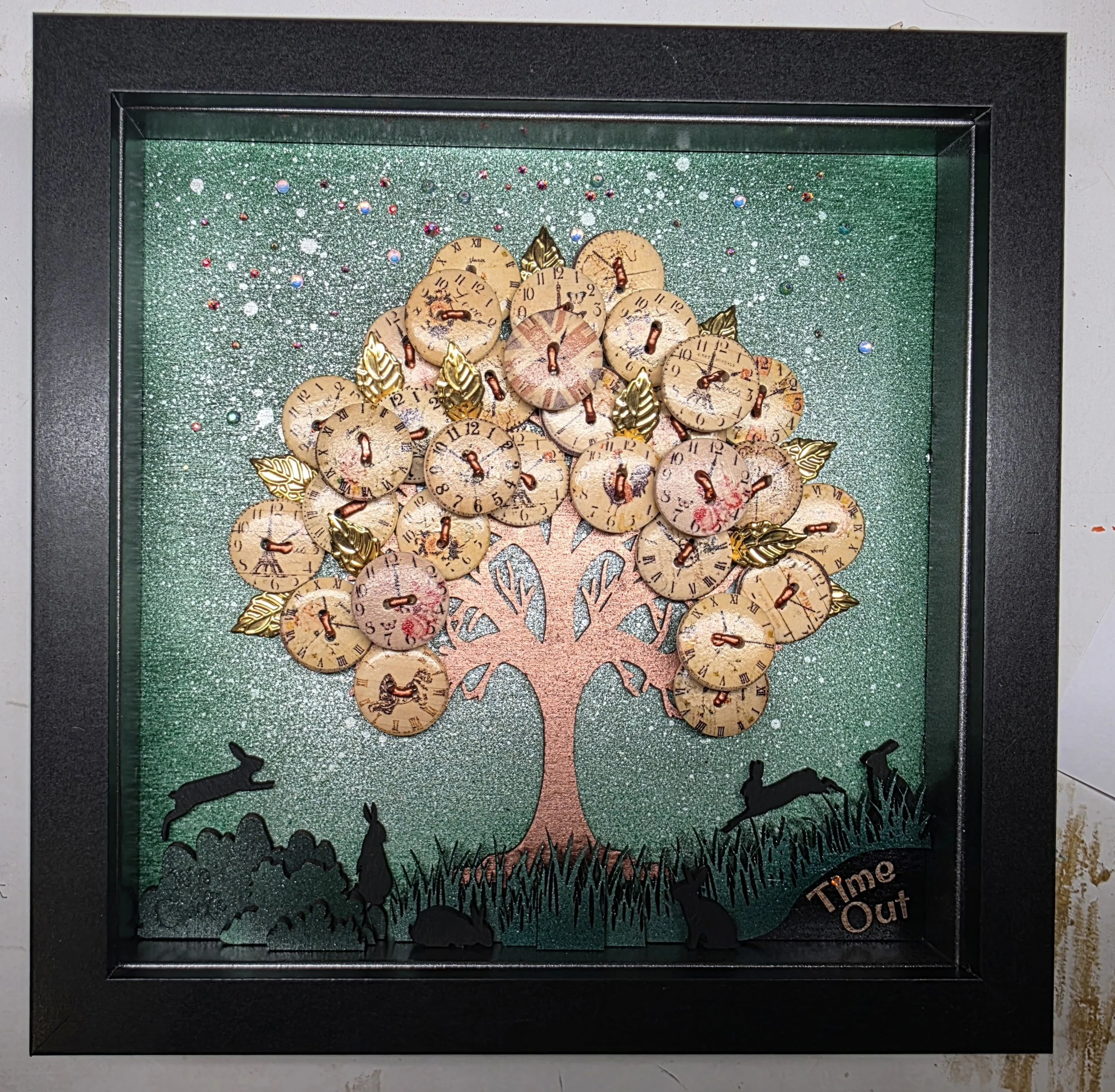 Decorative shadow box featuring a textured background with glitter, arranged vintage clock faces, metallic gold leaves, and cut-out silhouette of children playing, with the phrase 'Time Out' at the bottom.