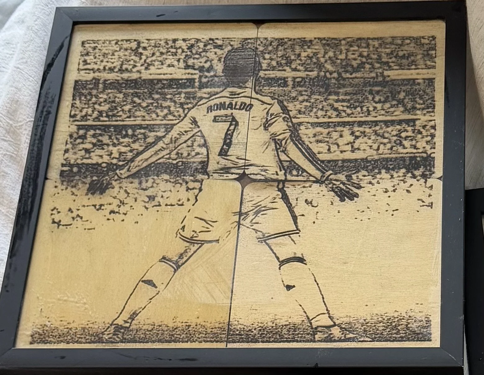 Wooden artwork depicting soccer player Cristiano Ronaldo standing with arms outstretched, viewed from the back, in a stadium.