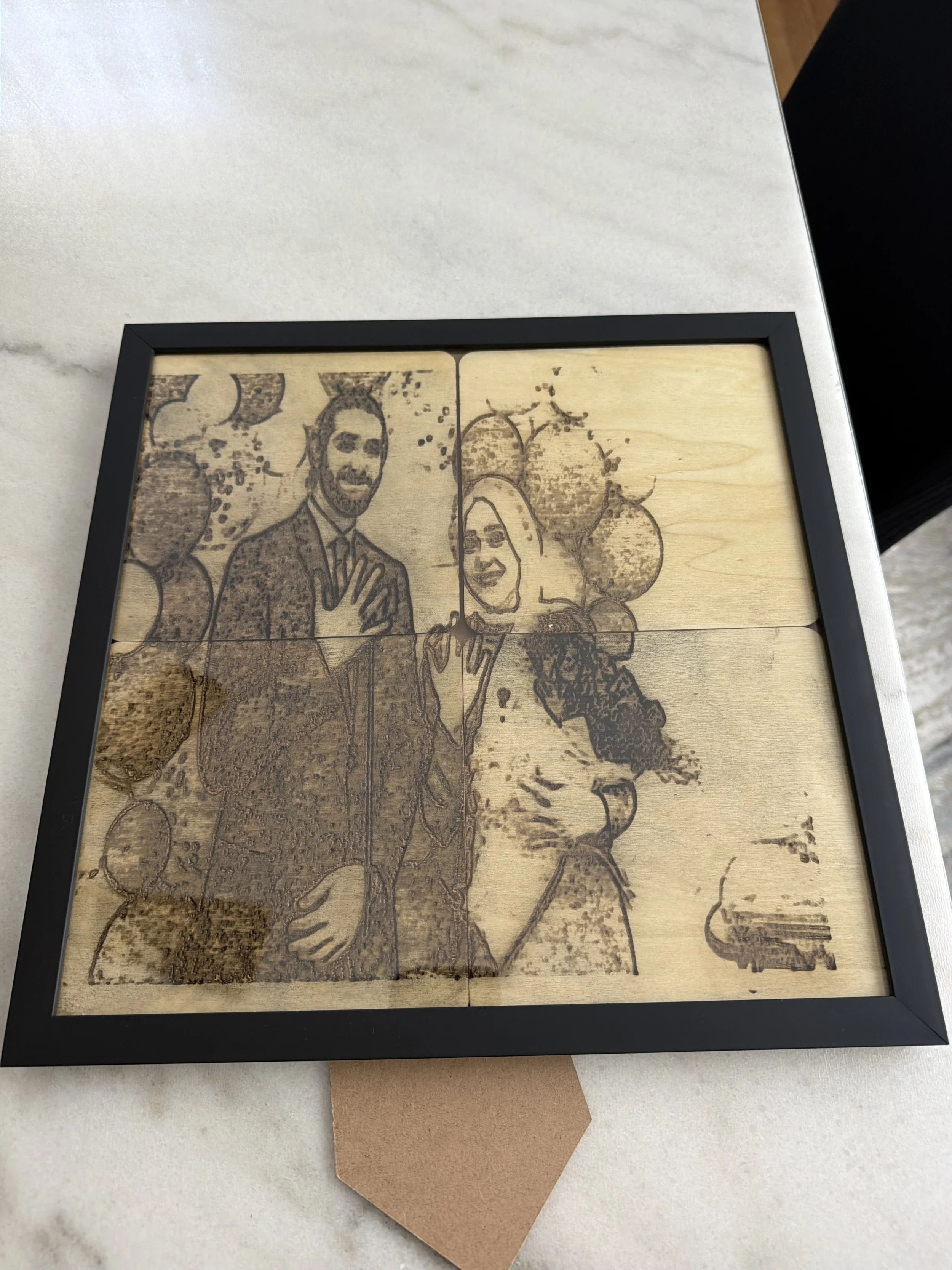 A framed wooden artwork depicting a man in a suit and a woman with balloons in the background.
