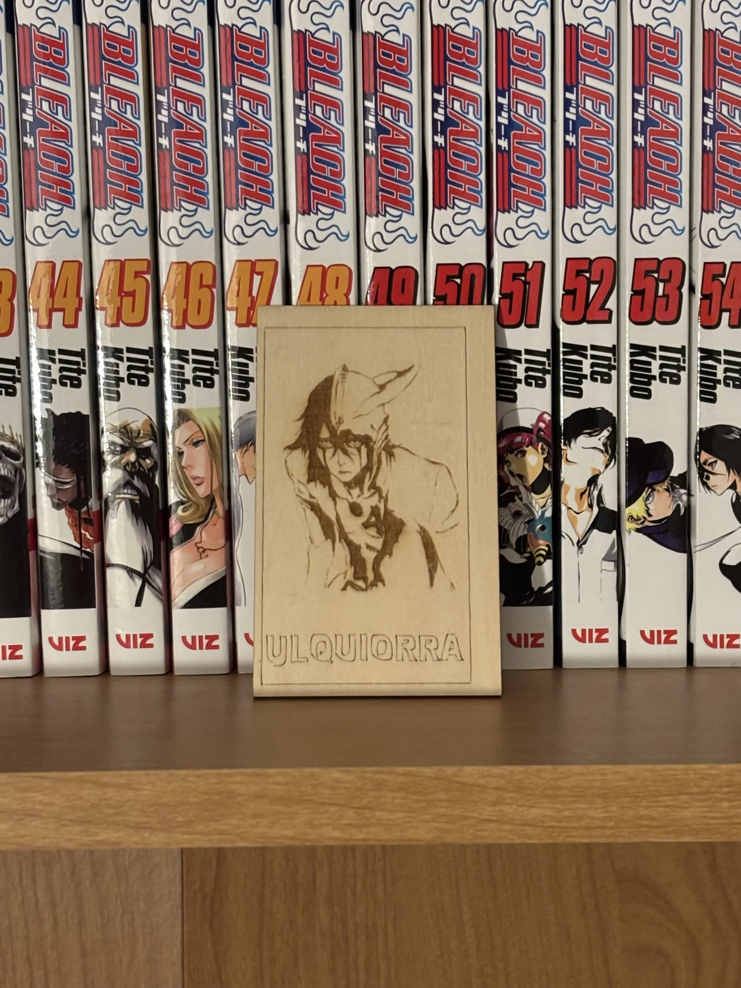 Collection of comic books titled 'The Amazing', arranged vertically with numbered spines from 1 to 54, along with a wooden plaque with a sketch of a person and the name 'Ulquiorra'.