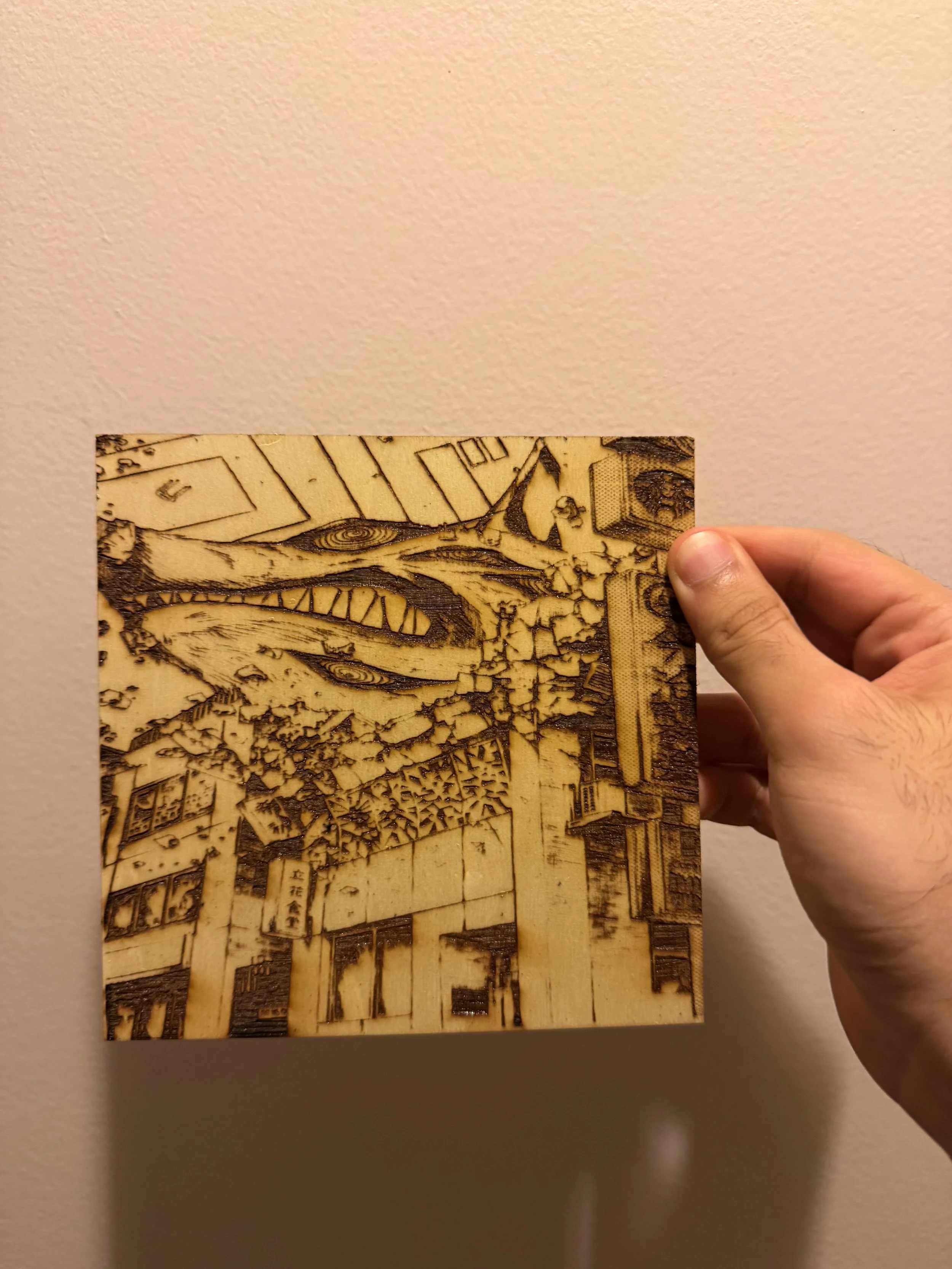 Person holding a wooden art piece with a detailed scene, standing against a plain wall.