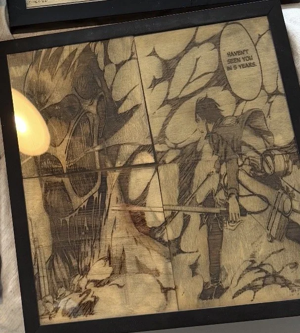 A framed artwork or print depicting a comic-style scene with two characters. One character, on the right, appears to be a man with dark hair, dressed in casual clothing, holding a leash attached to a dog. The other character, on the left, has long ha