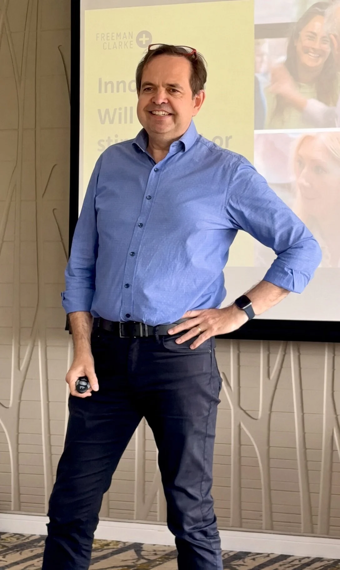 Gerry Lawrence in a blue shirt, standing in front of a presentation screen, giving a talk for Freeman Clarke at a Gatwick Diamond Business event.