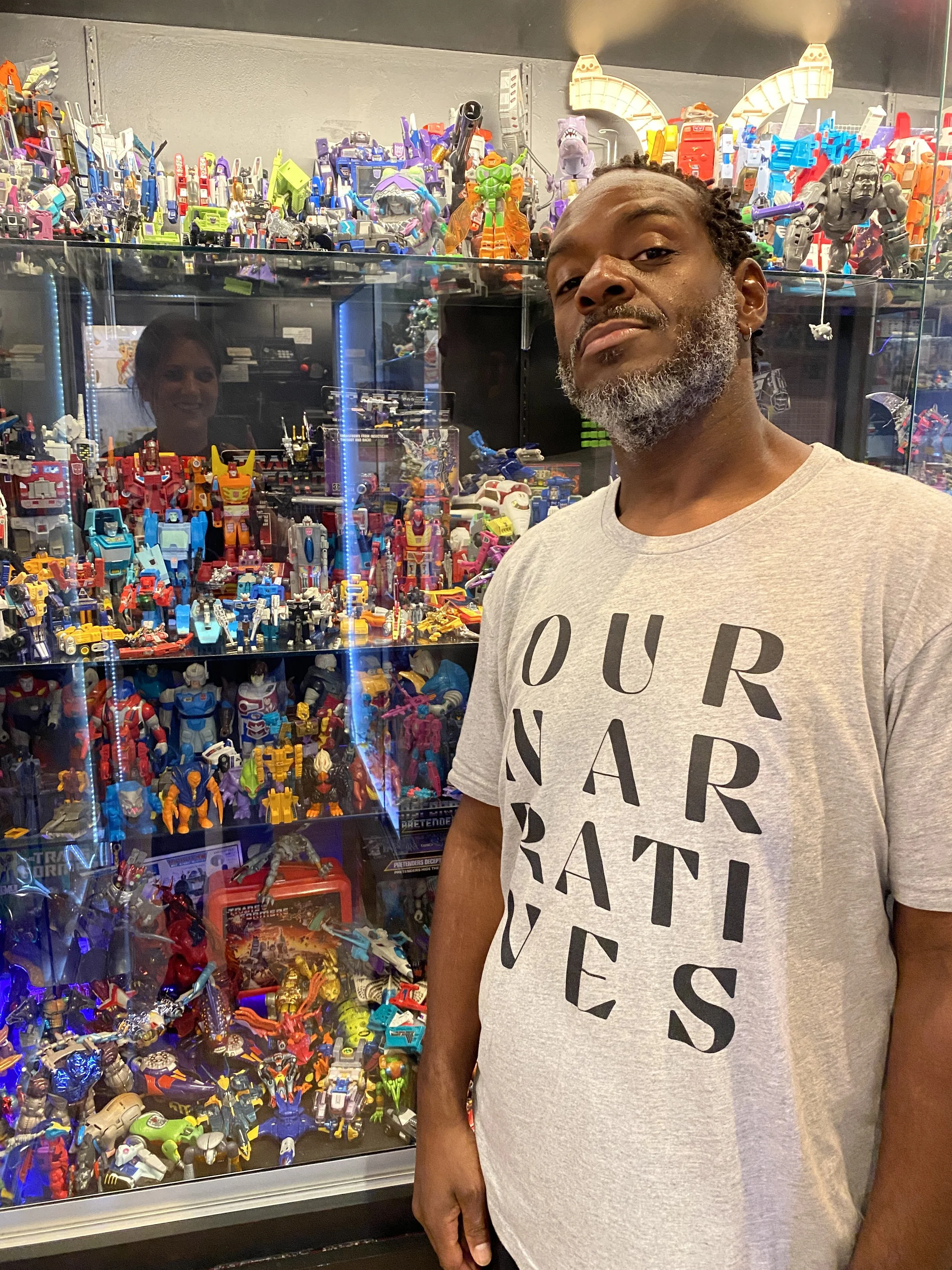 A man standing in front of a display case filled with a collection of colorful Transformers toys and action figures.