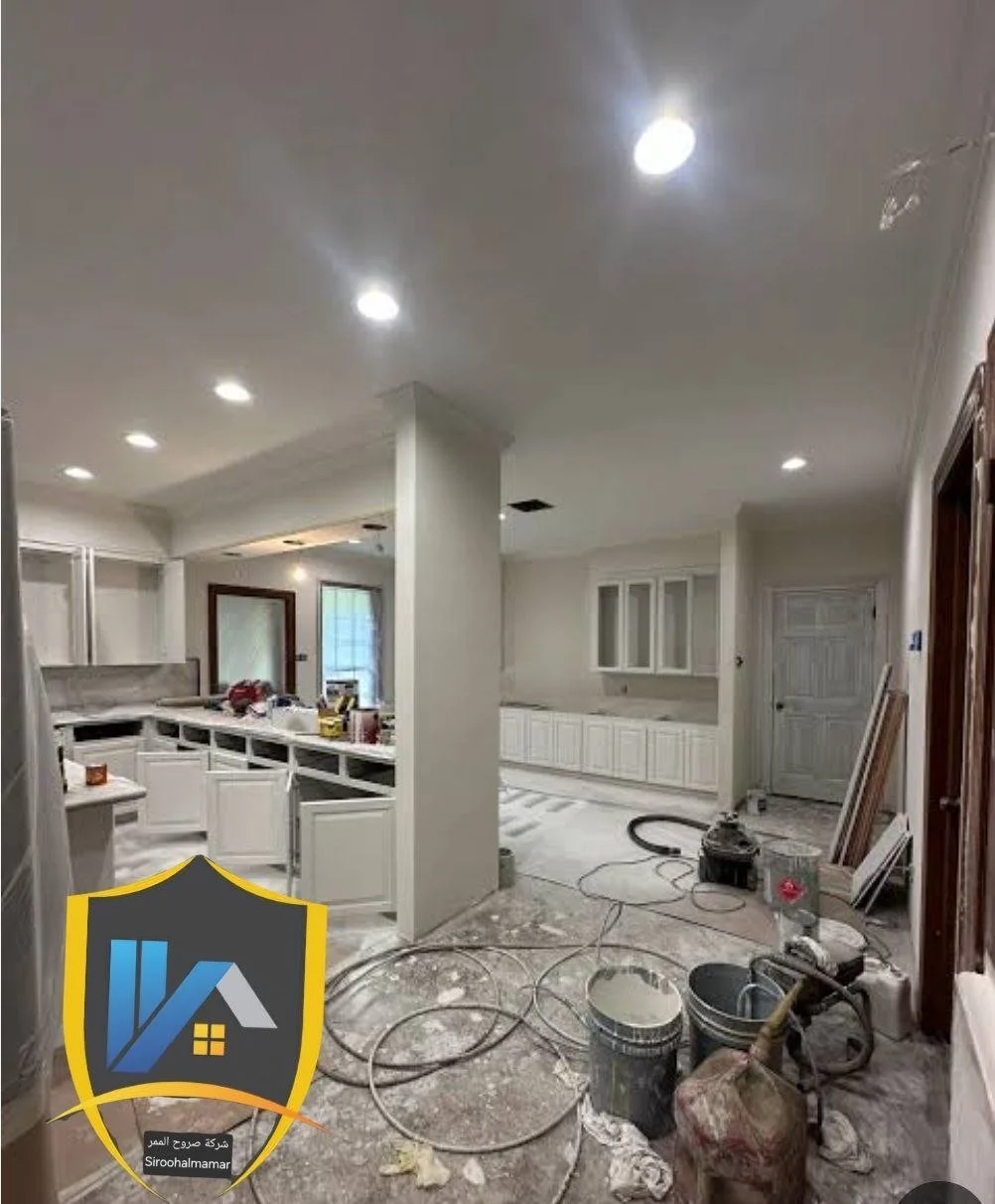 Kitchen area under renovation with construction tools on the floor, white cabinets, and recessed ceiling lights.