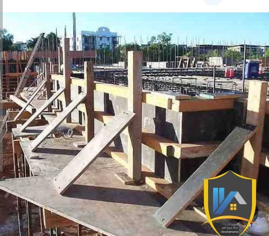 Construction site with wooden formwork for concrete stairs and walls, steel reinforcements, and scaffolding in the background.