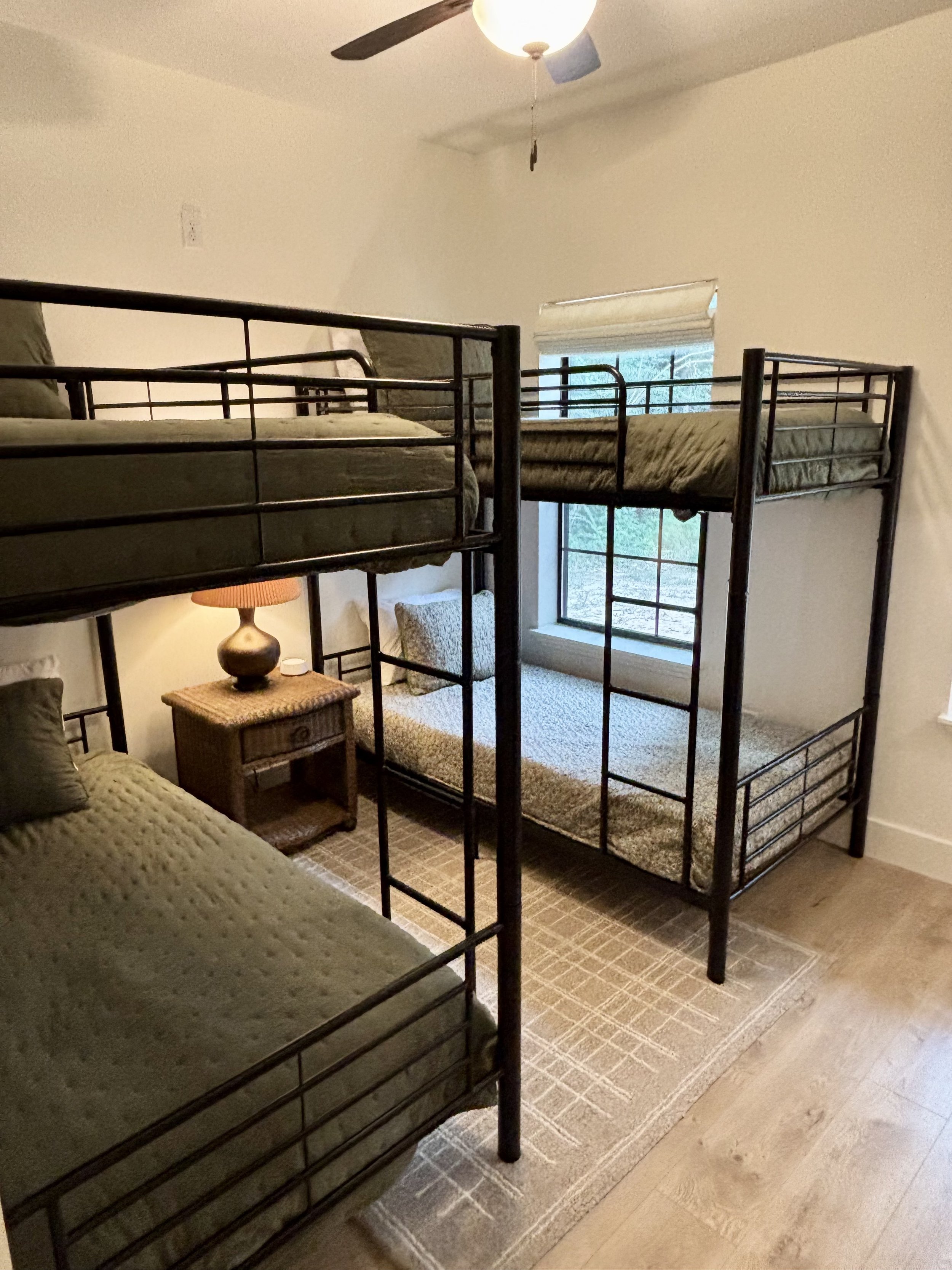 Bunk beds in a bedroom with a window, a nightstand with a lamp, and a beige rug.