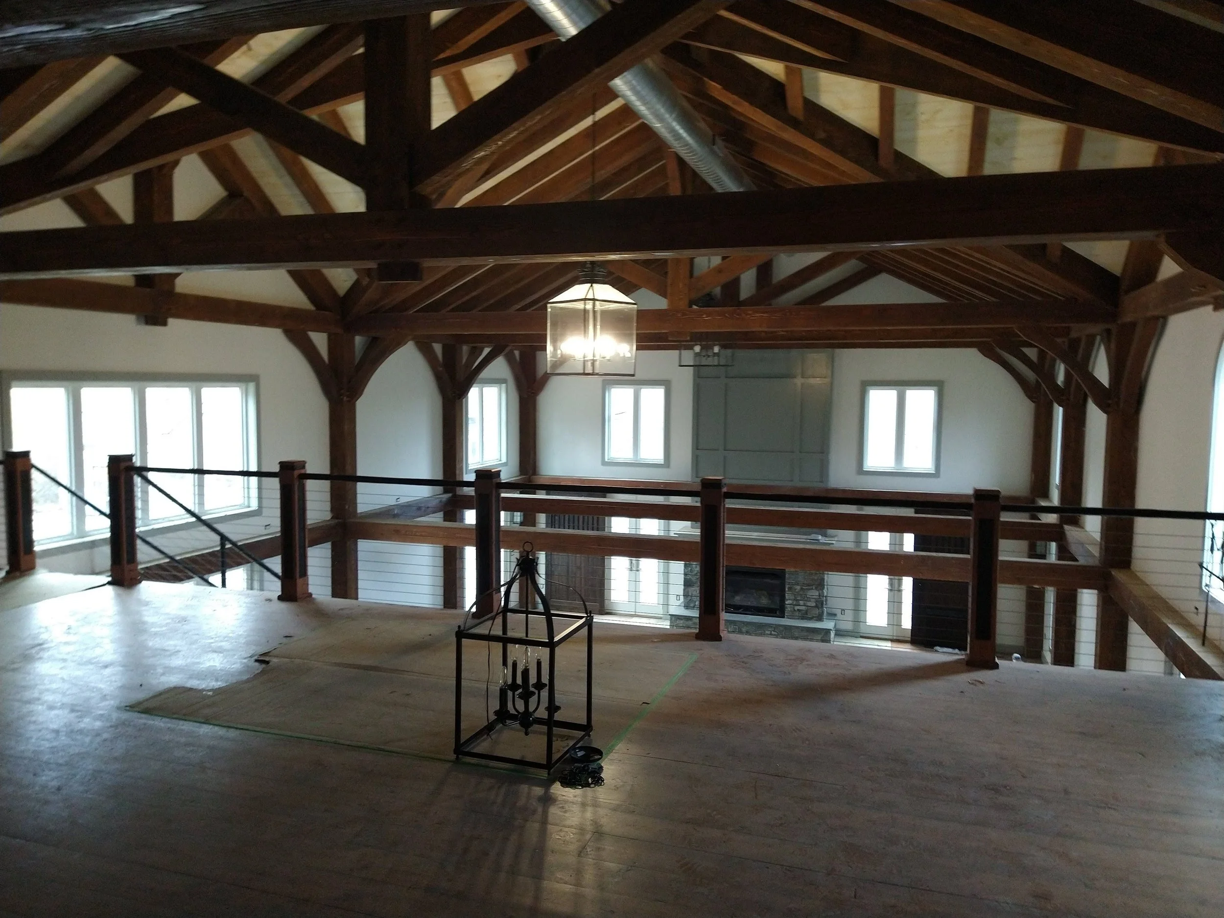 Interior of a spacious, open-concept room with high vaulted wooden ceilings, exposed wooden beams, multiple windows, and a wooden balcony railing overlooking the lower level.