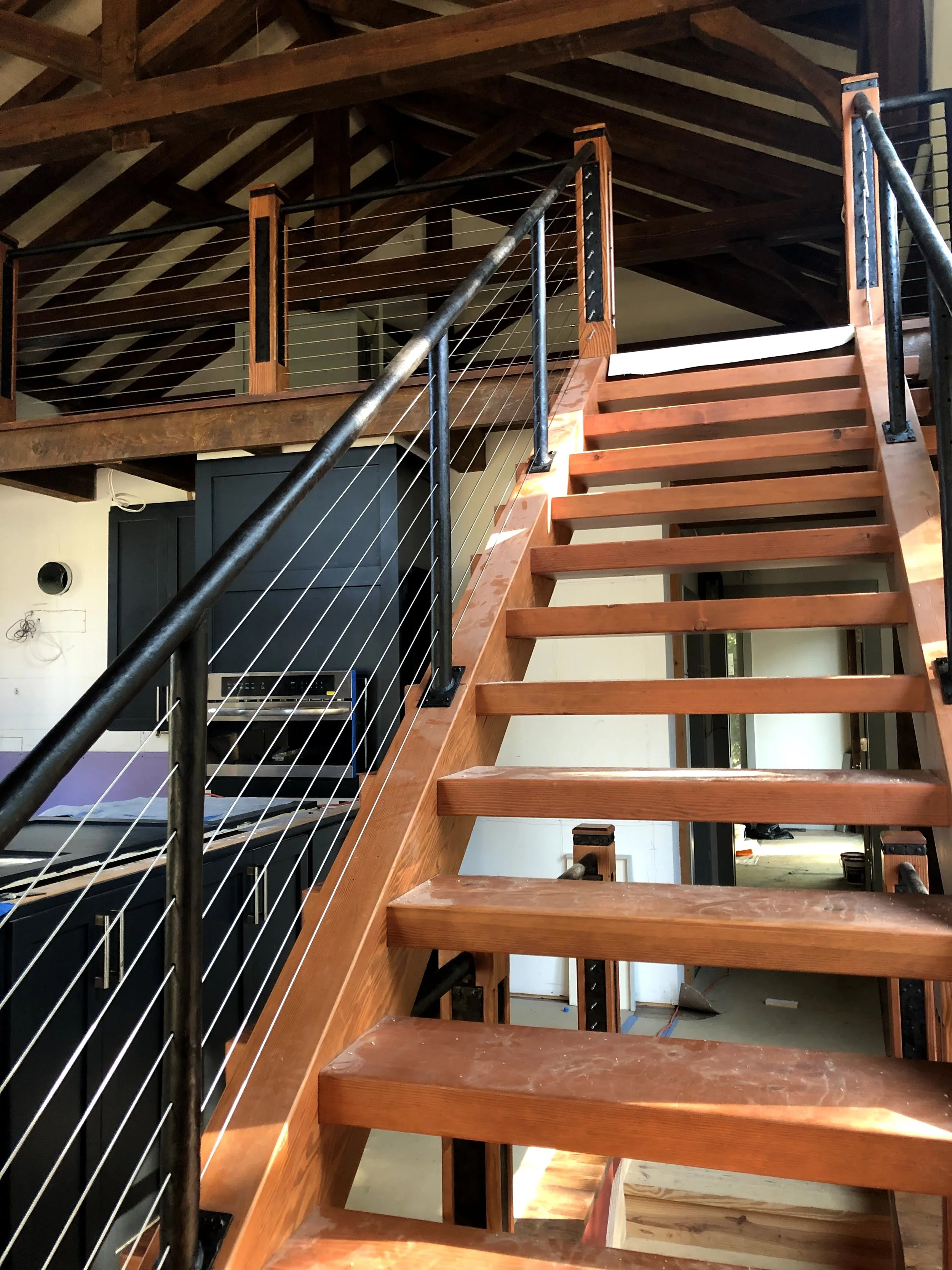 Interior of a house under construction with a wooden staircase and loft area. The staircase has wooden steps and metal railing.