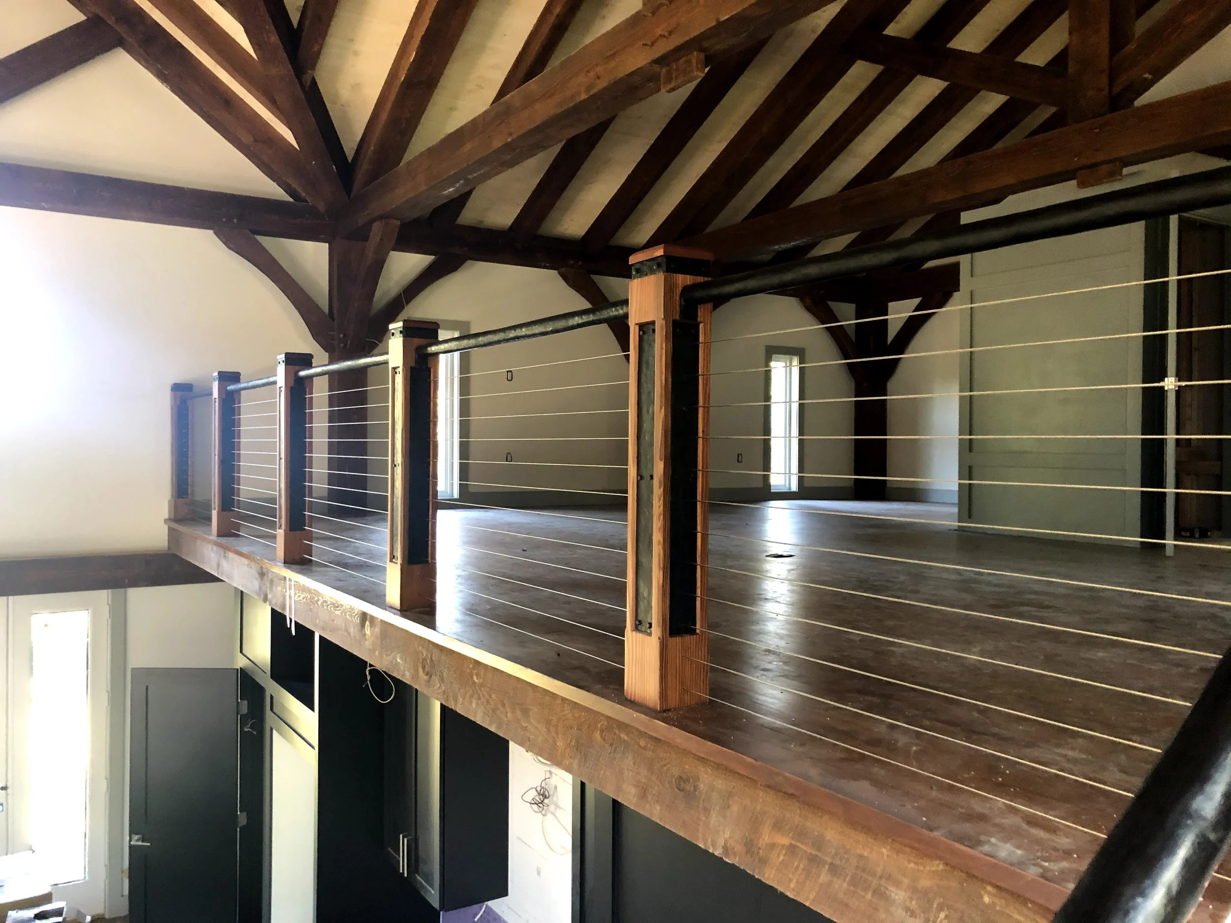 Interior view of a room with wooden beams on the ceiling, a wooden floor, and a cable railing with horizontal wire cables and custom newel posts.