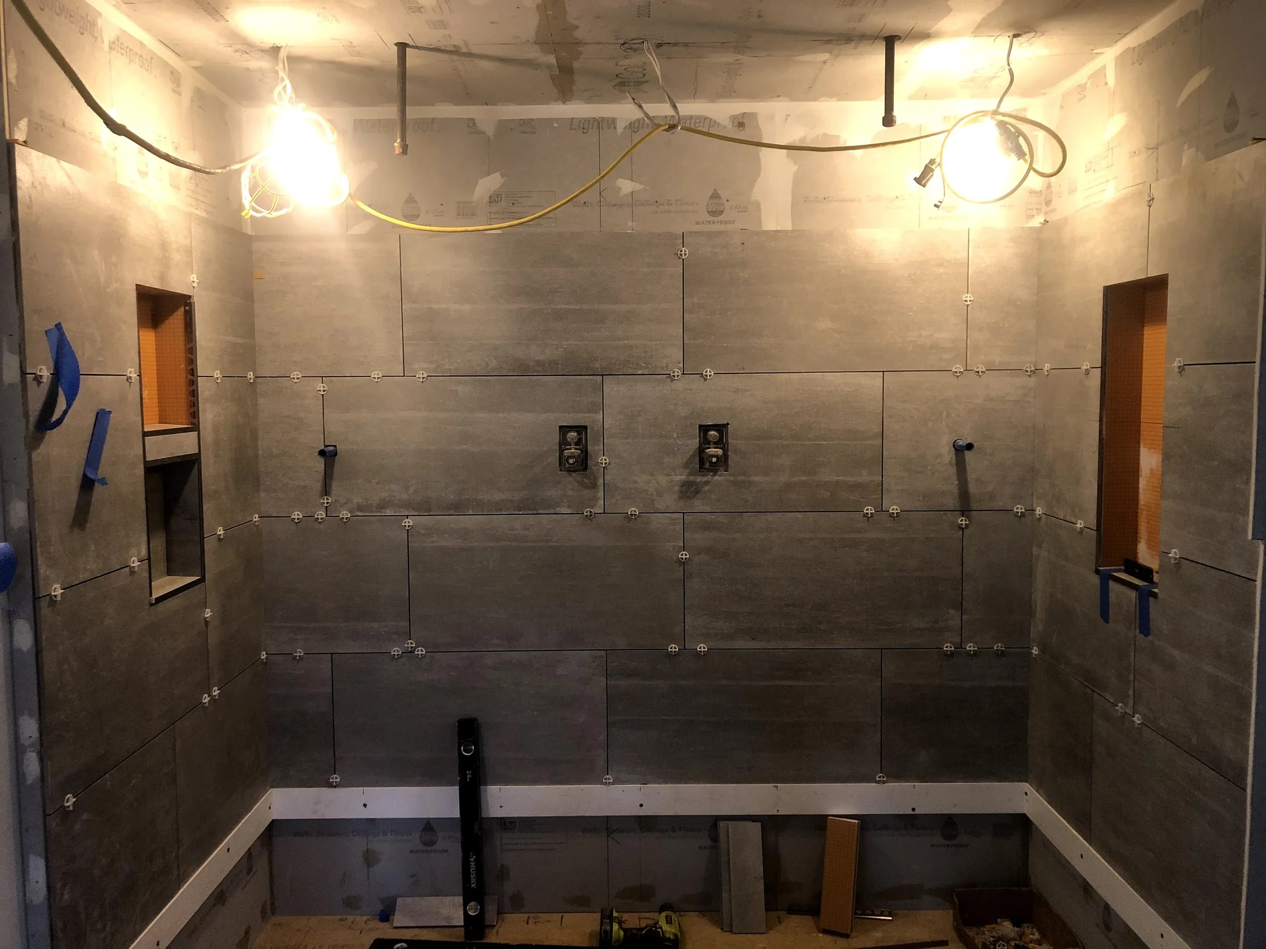 Bathroom under construction with tiled walls, electrical wiring, and lighting fixtures being installed.