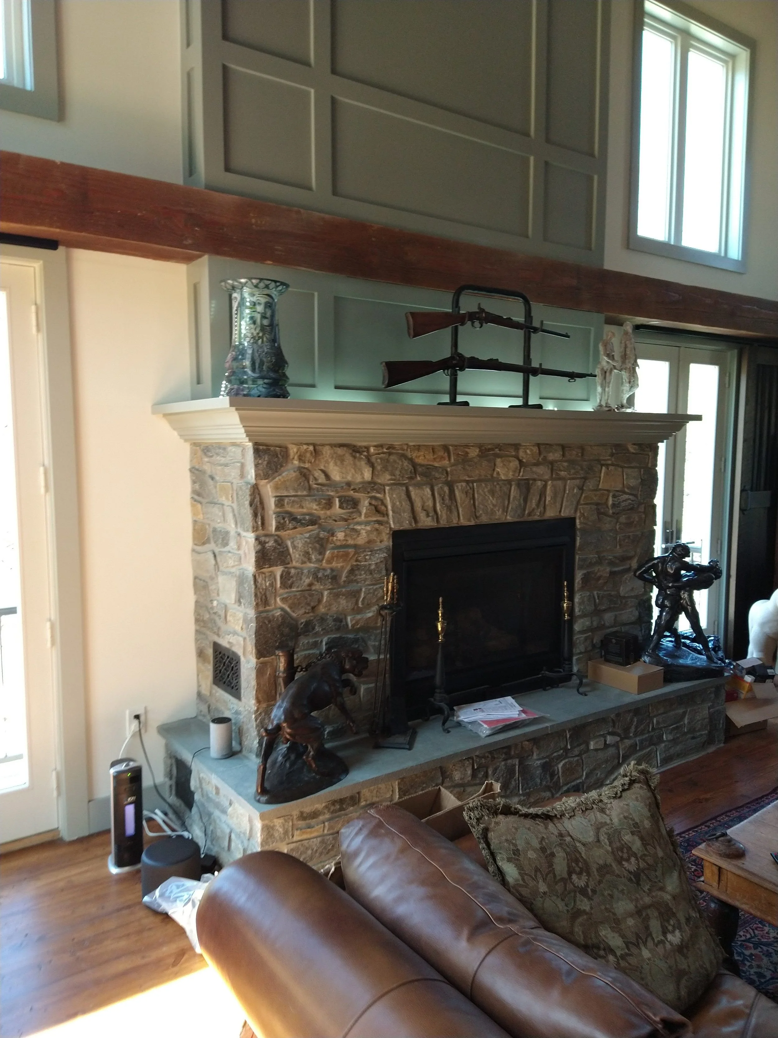 A living room fireplace with decorative statues and rifles on the mantel, and a leather sofa in the foreground.