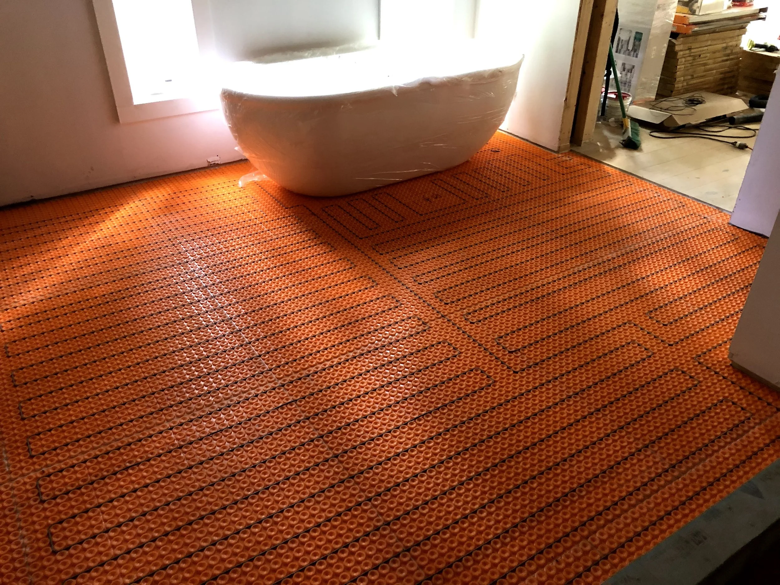 Bathroom under construction with schluter ditra under floor heating sub flooring, and a white Japanese style soaking tub near a door..