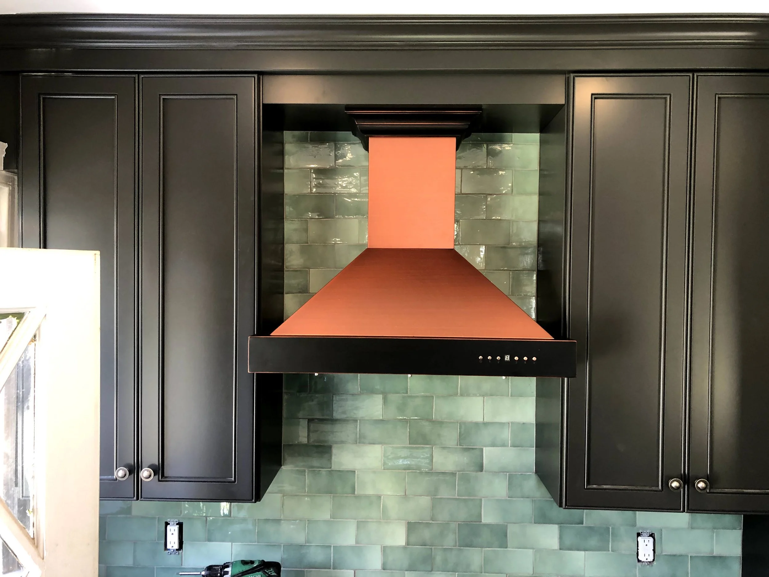Kitchen with dark cabinets, green tile backsplash, and a copper range hood