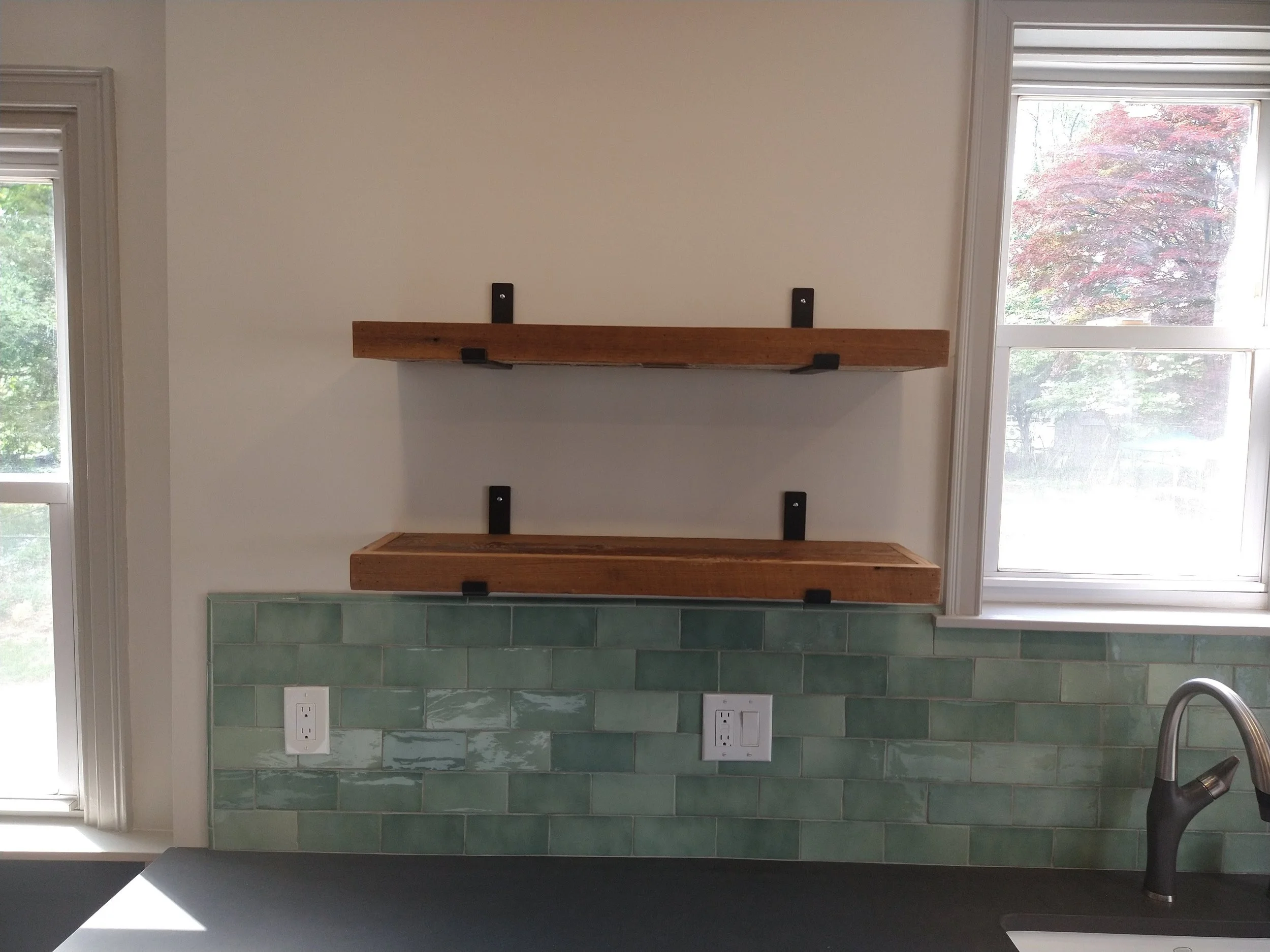 Kitchen with green tile backsplash, wooden floating shelves, and modern faucet.