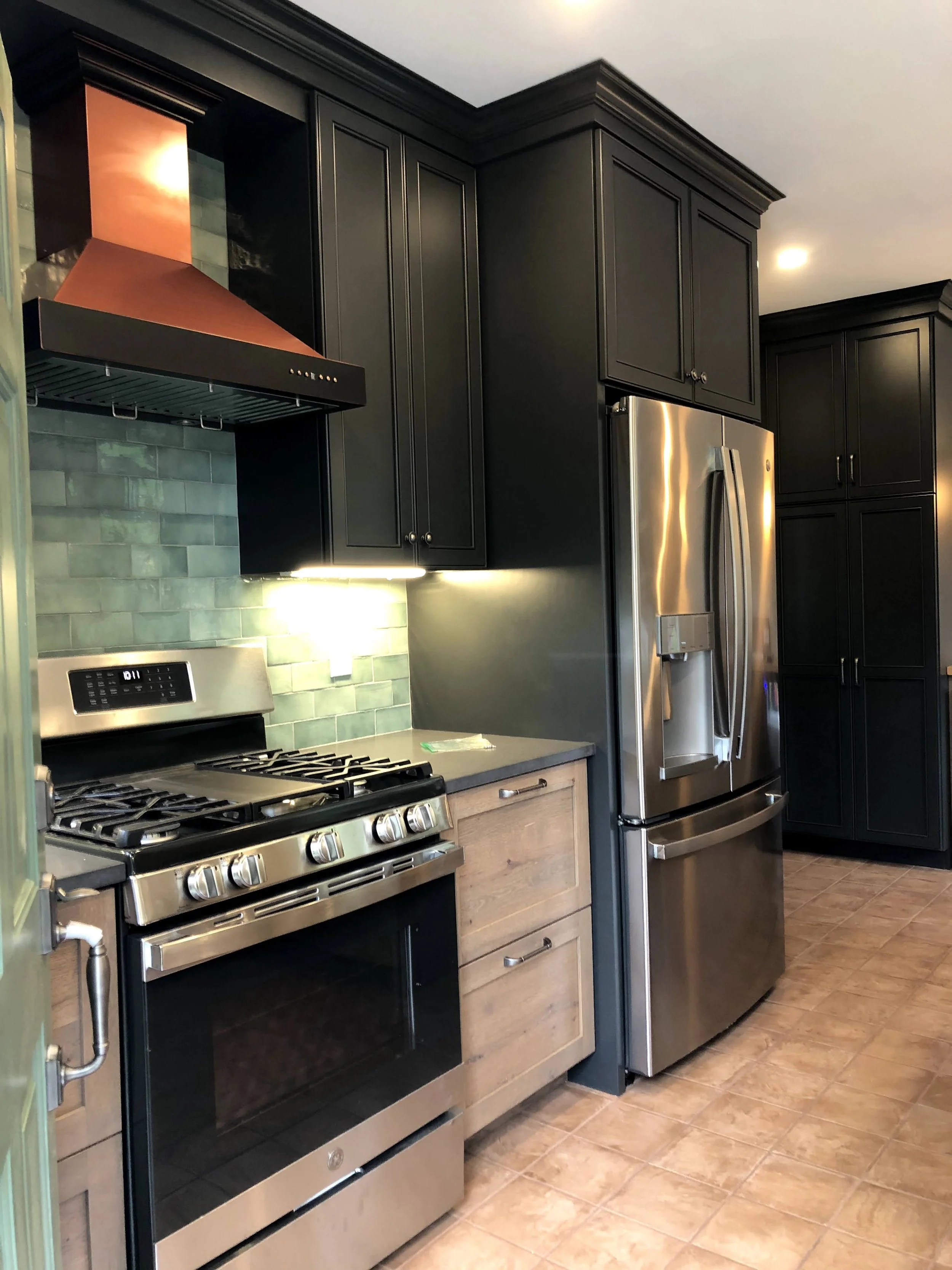 Modern kitchen with stainless steel appliances, dark cabinets, green tile backsplash, stainless steel refrigerator, stove, and copper range hood.