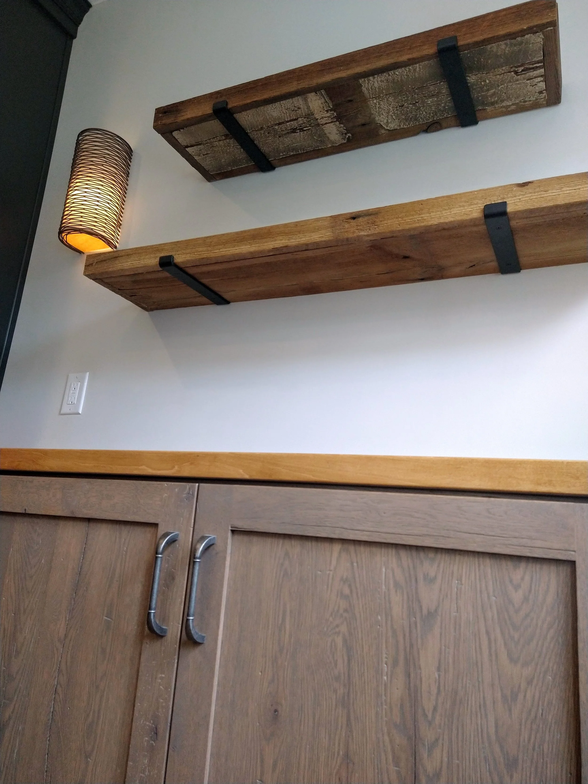 Wooden shelves with metal brackets, wooden cabinet with metal handles, and a wall sconce light fixture.