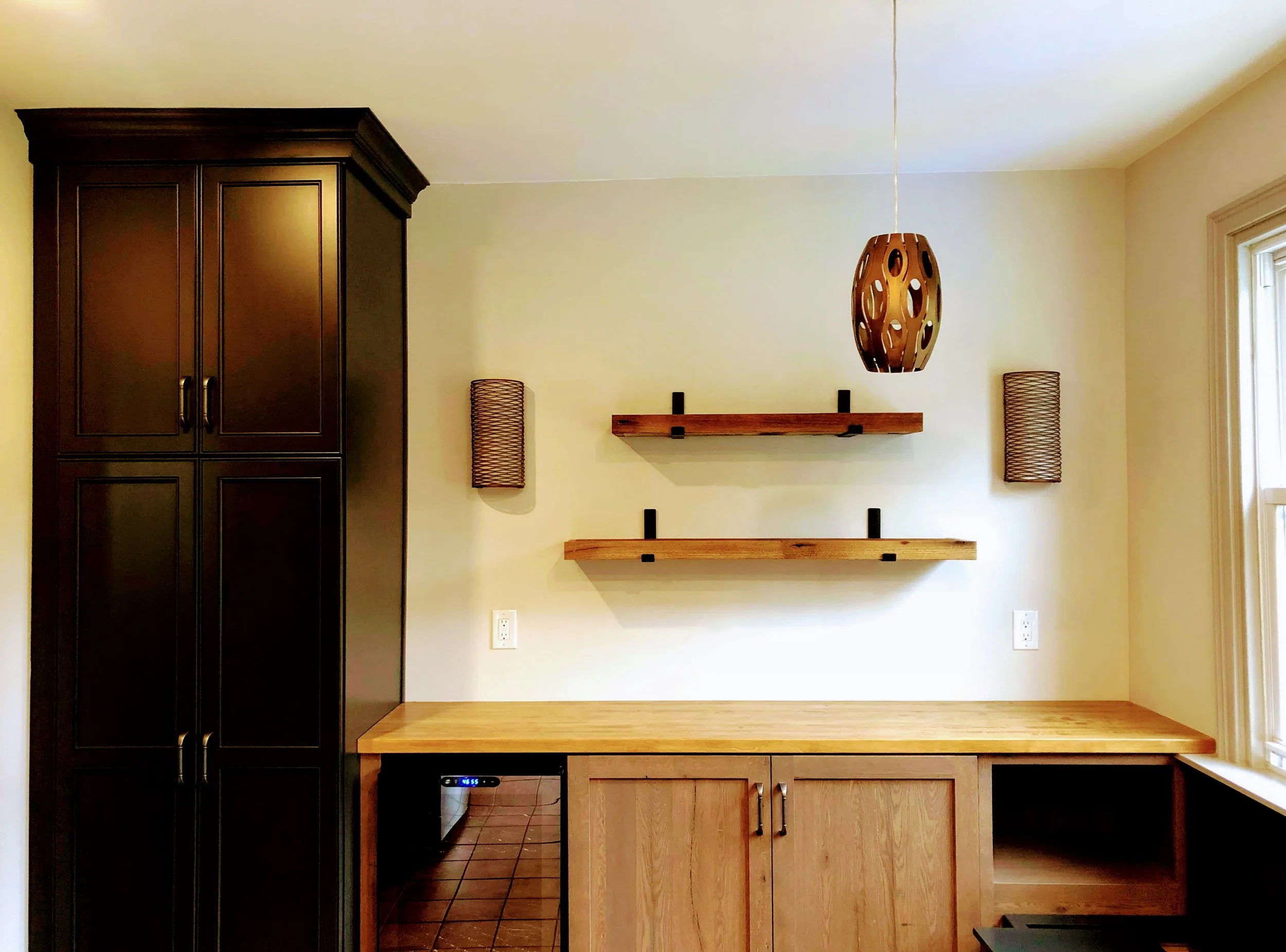 Modern kitchen interior with dark cabinets, wooden countertop, floating shelves, and hanging pendant light.