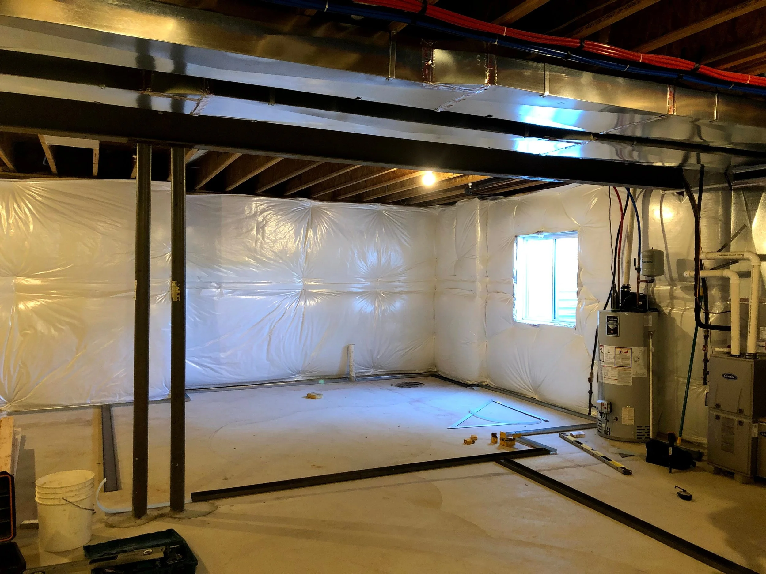 Unfinished basement with insulation on the walls and construction tools on the floor.