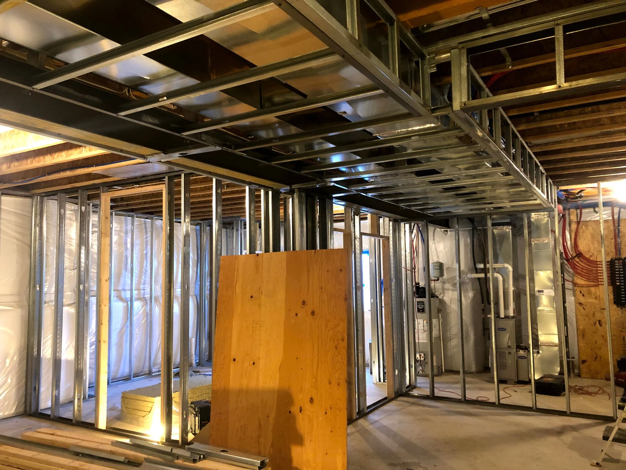 Interior view of a construction site with metal framing for walls and ceiling, electrical wiring, and insulation materials being installed.