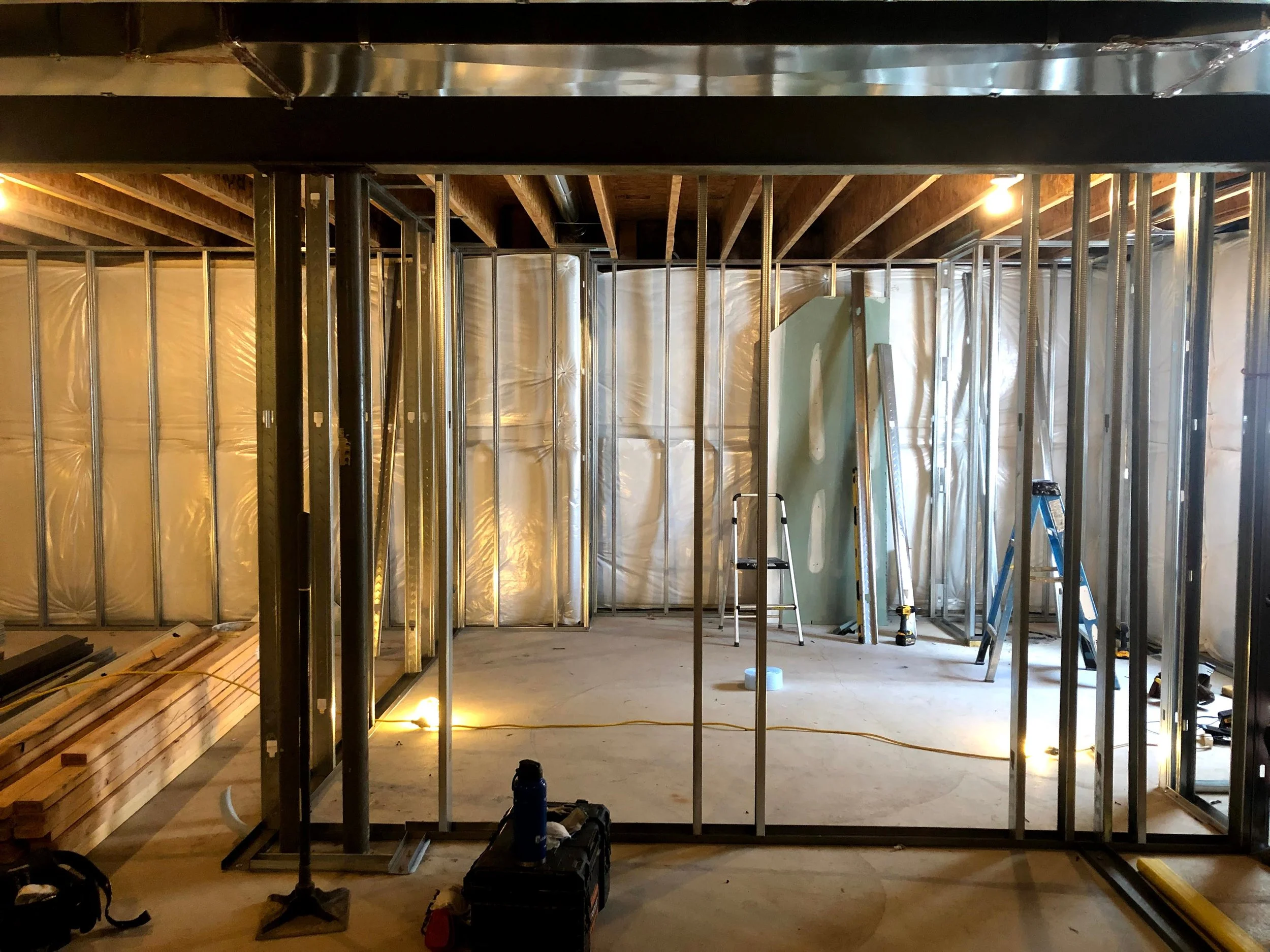 Construction site showing metal framing for walls in an unfinished room, with tools and ladders scattered around.