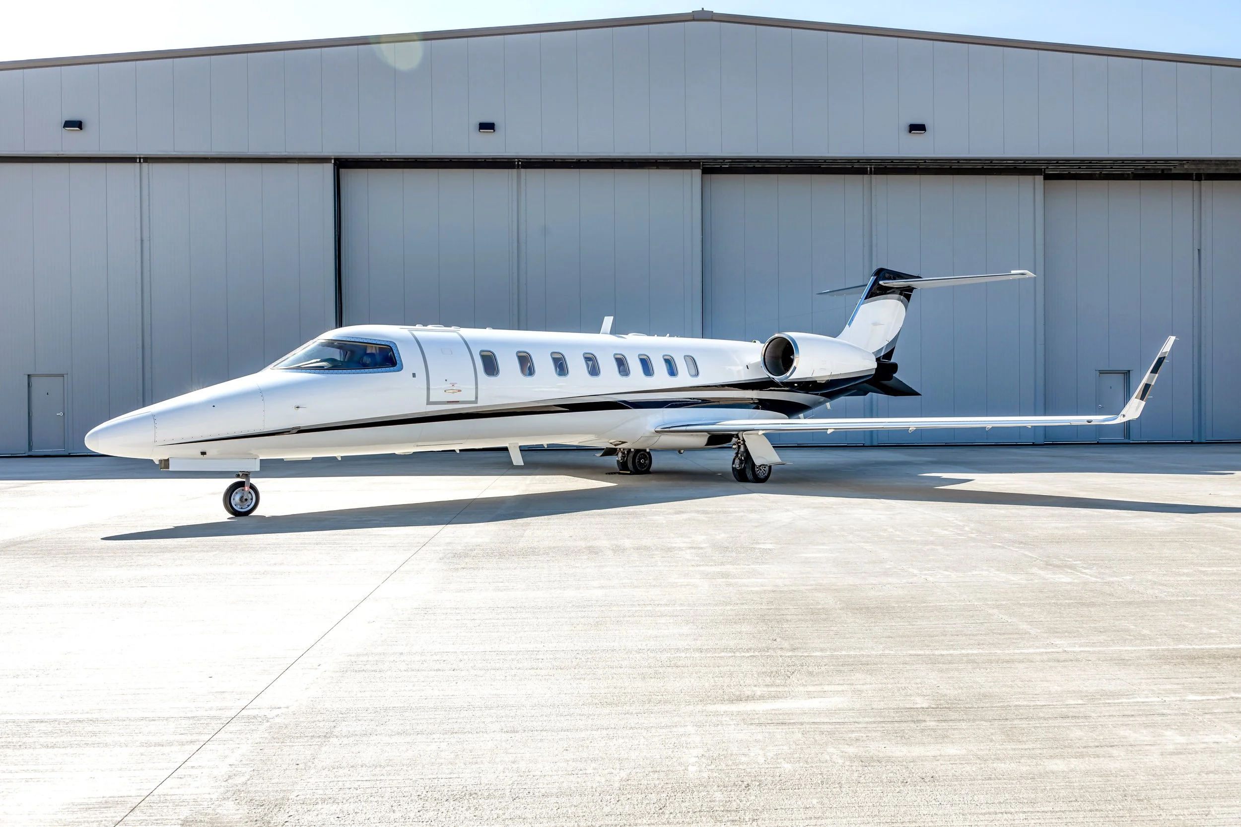 Private jet parked on a tarmac in front of a hangar under a clear blue sky.