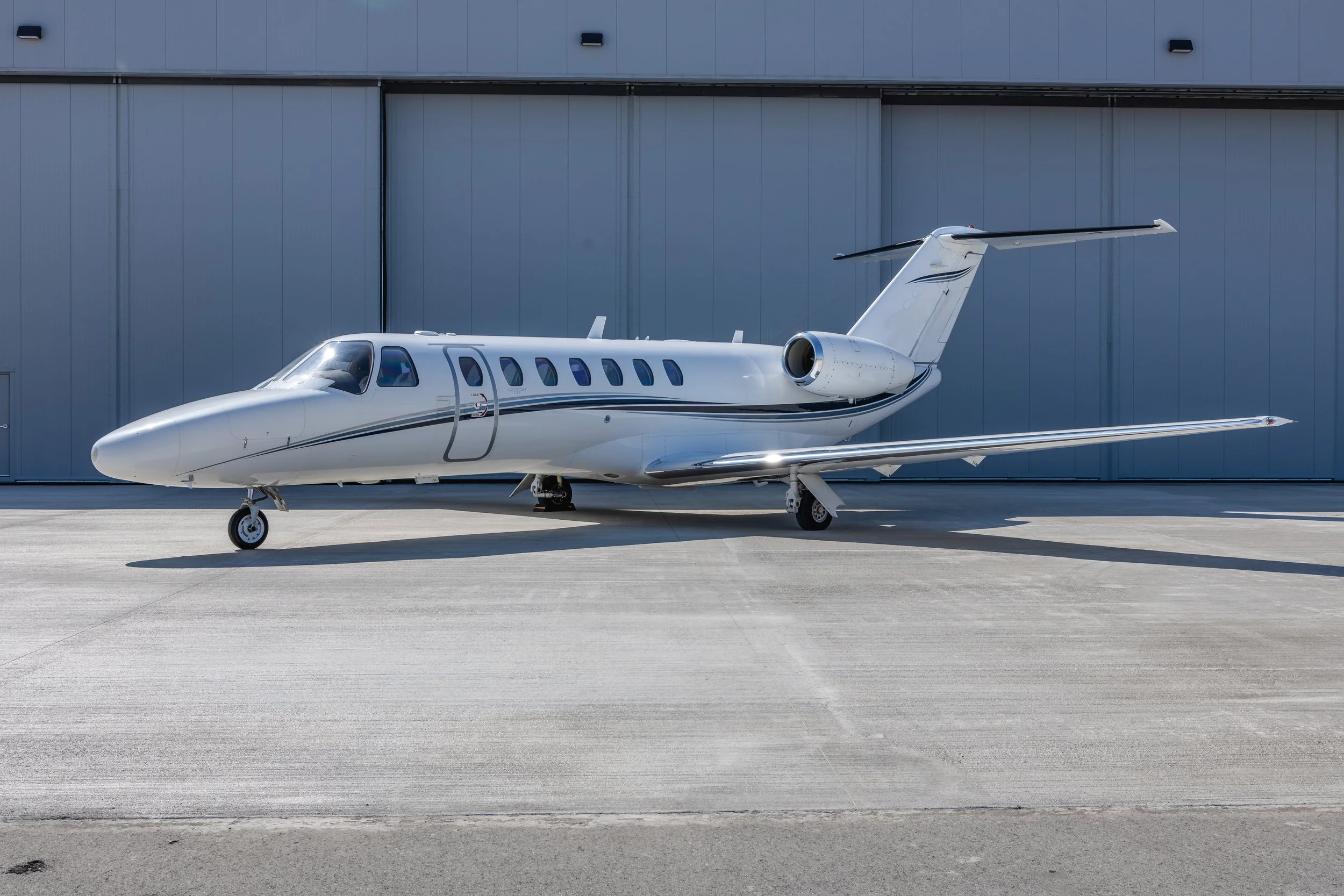 A white private jet parked on a concrete tarmac near a large gray hangar.