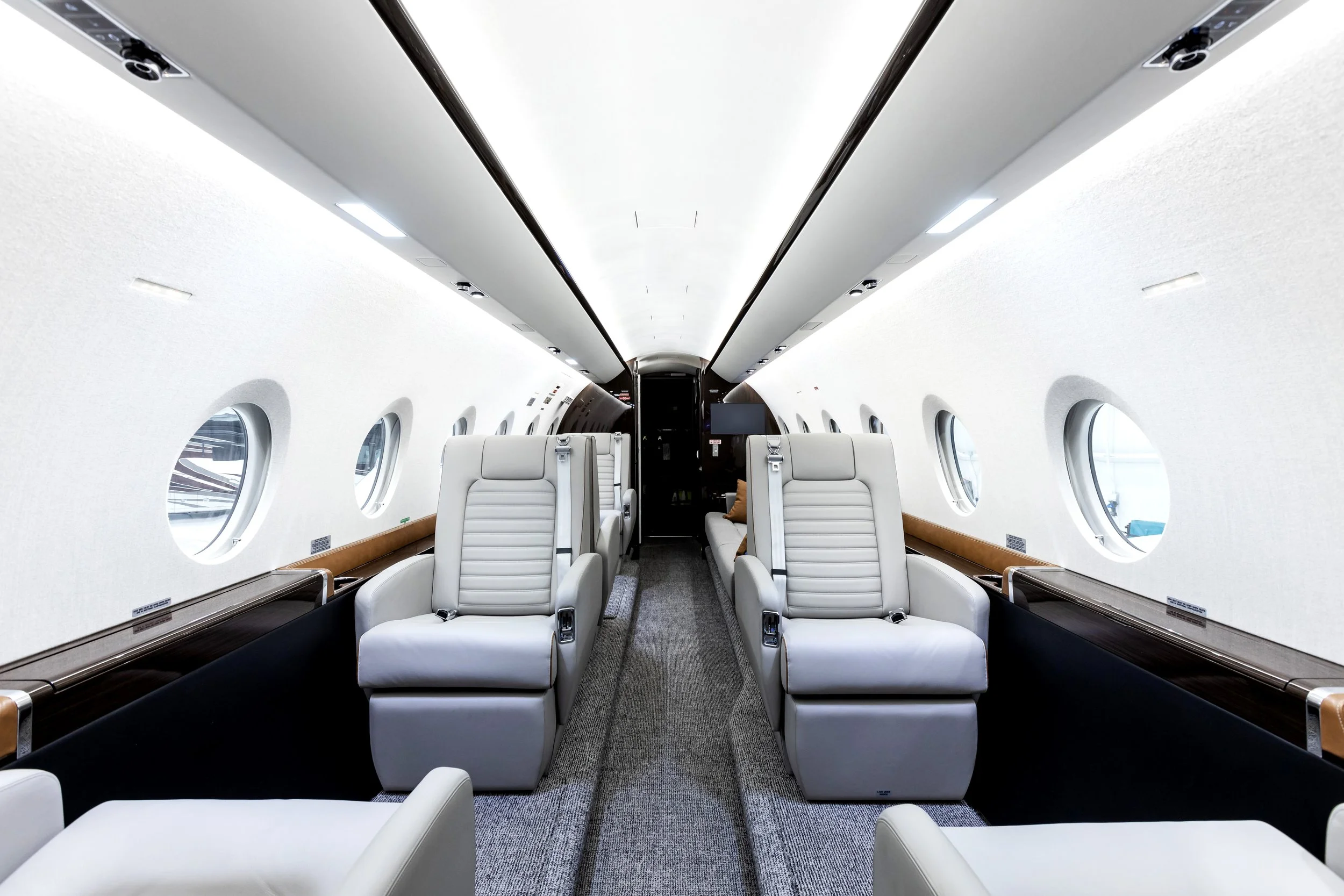 Interior of an airplane cabin with white leather seats arranged in rows, windows along the sides, and overhead lighting.